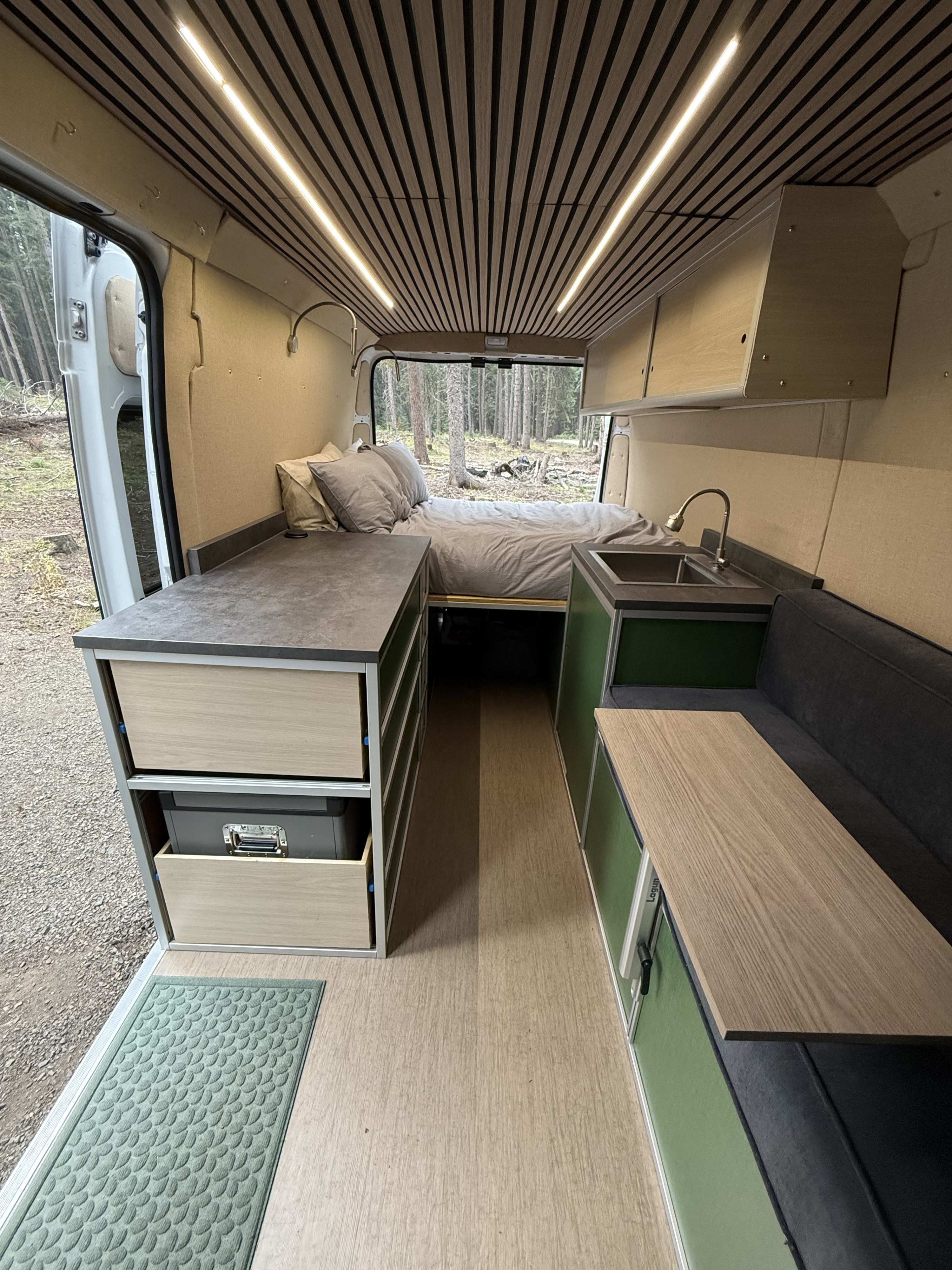 Inside a modern rv rental, featuring a comfortable rear bed, full kitchen, and flexible living space with wood accents.. Dodge B Van 2023