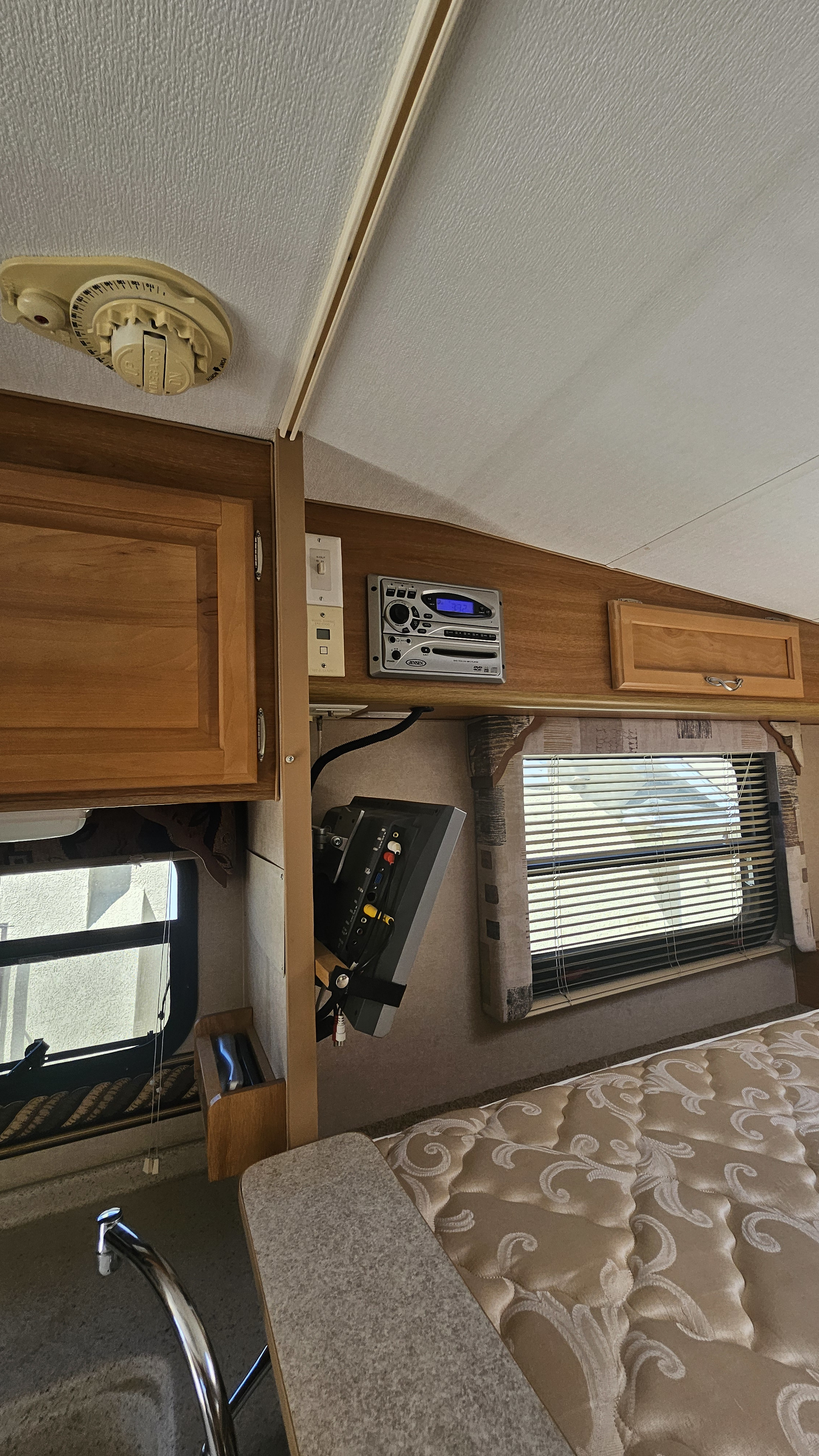 Inside a compact rv rental: wood cabinetry, Jensen entertainment system, a window, patterned bed, and kitchen area.. Lance 861 2016