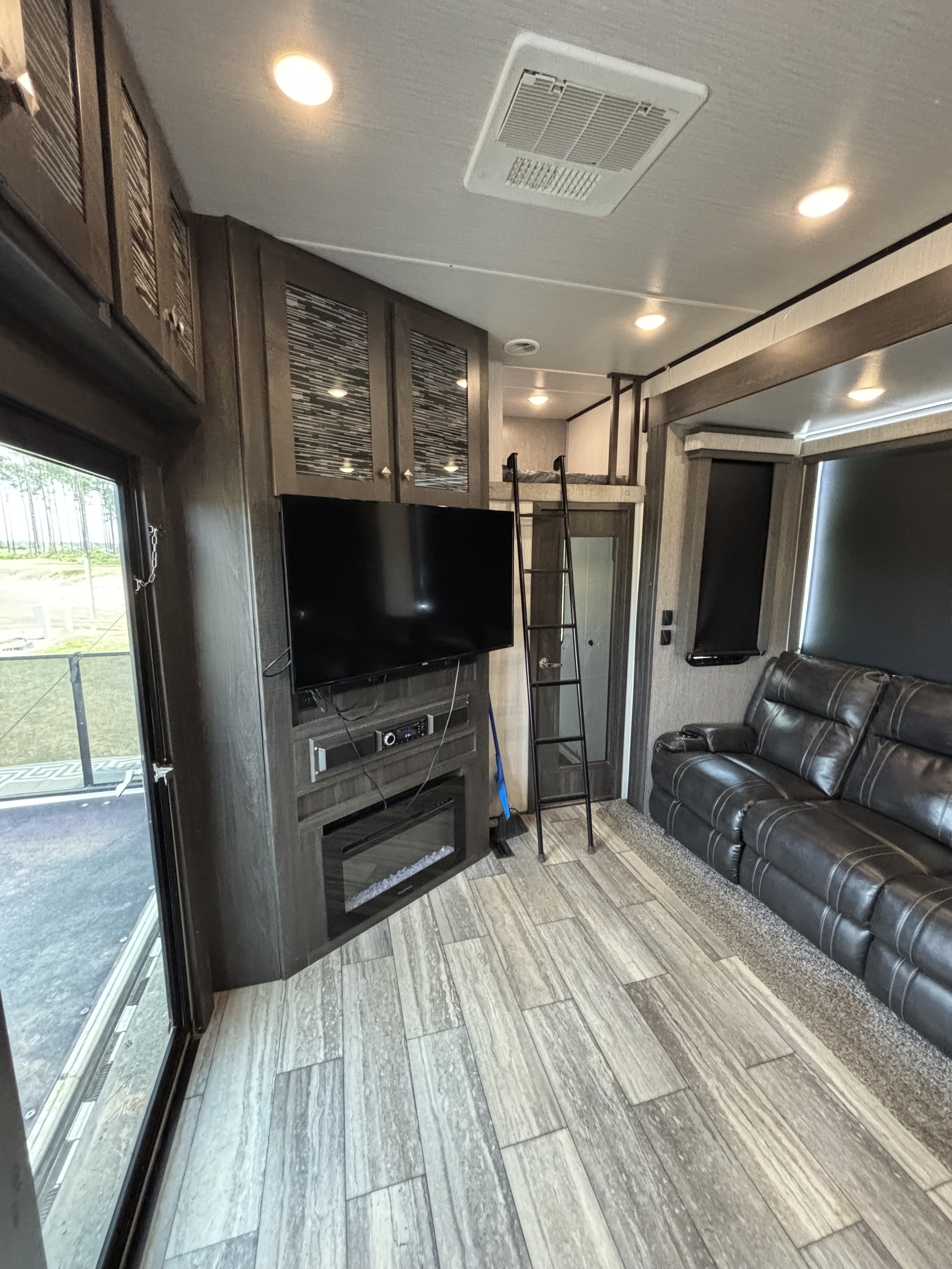 Modern RV rental interior with TV, fireplace, loft bed, and cozy sofa. Enjoy comfort and amenities for your travels.. Heartland Road Warrior 2020