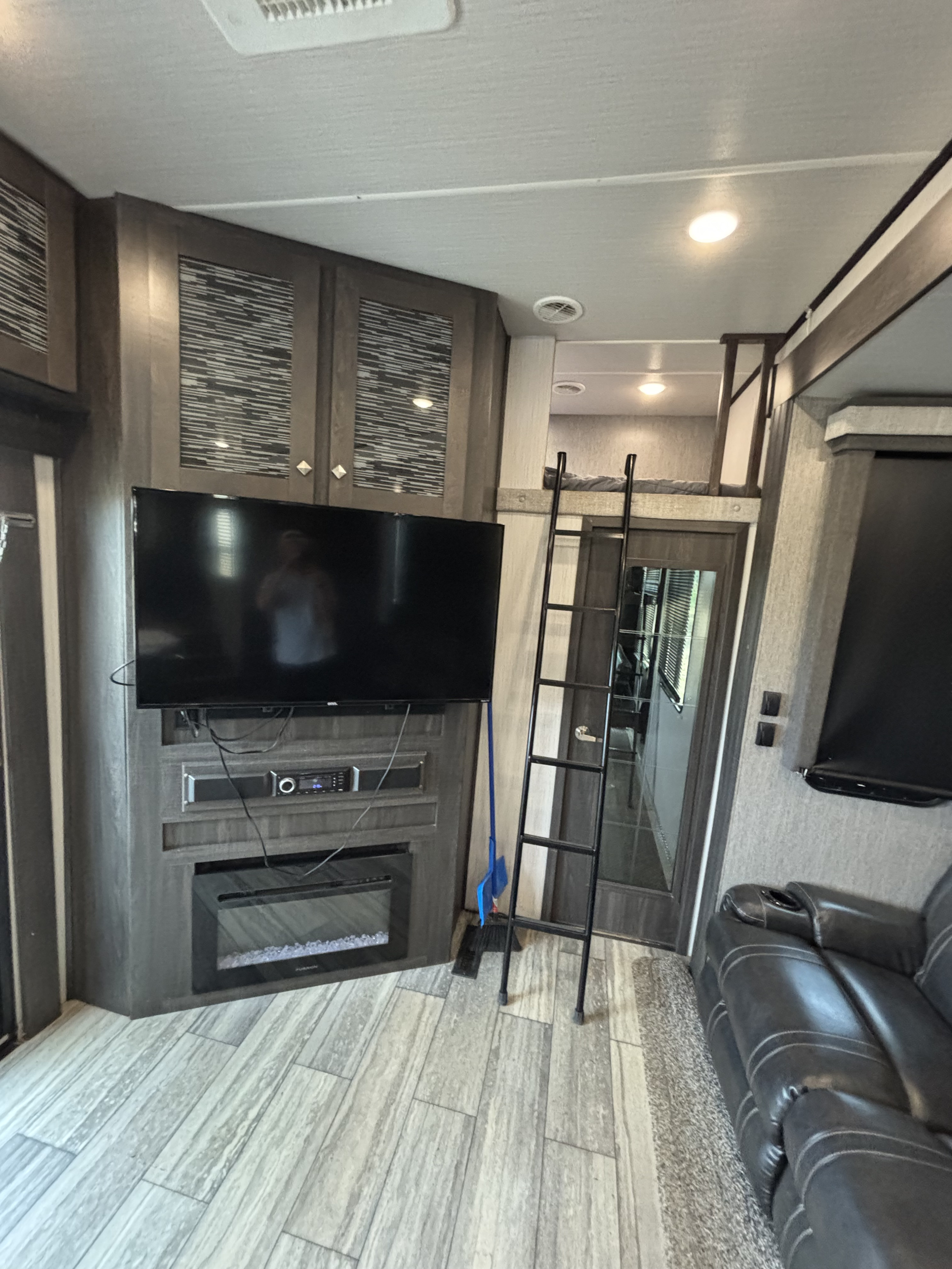 Modern RV rental living area featuring a TV, fireplace, ladder to bunk, and a comfortable leather sofa.. Heartland Road Warrior 2020