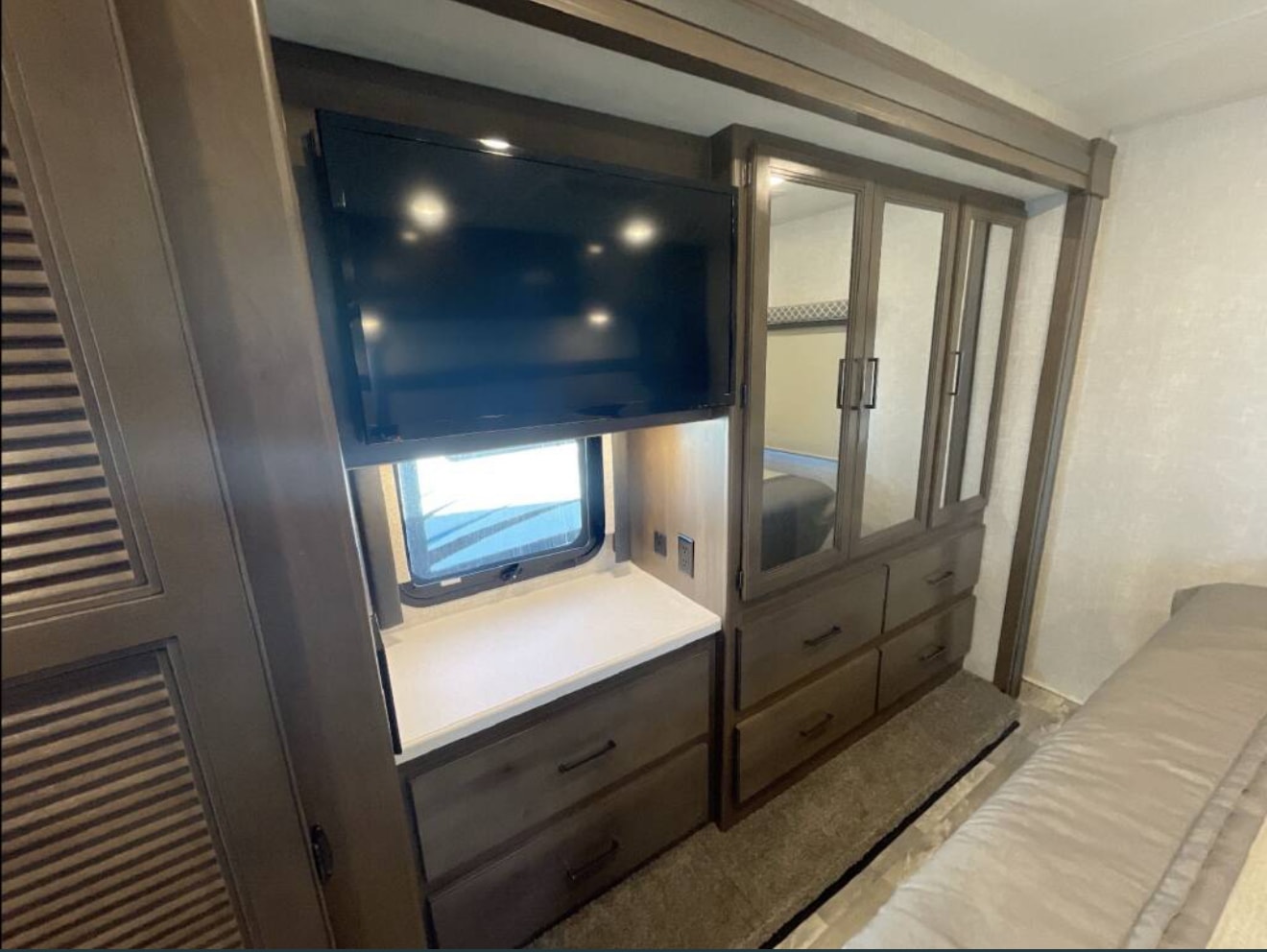 Modern RV rental interior showing a bedroom with mounted TV, mirrored wardrobe, ample storage, and a comfy bed.. Thor Windsport 2022