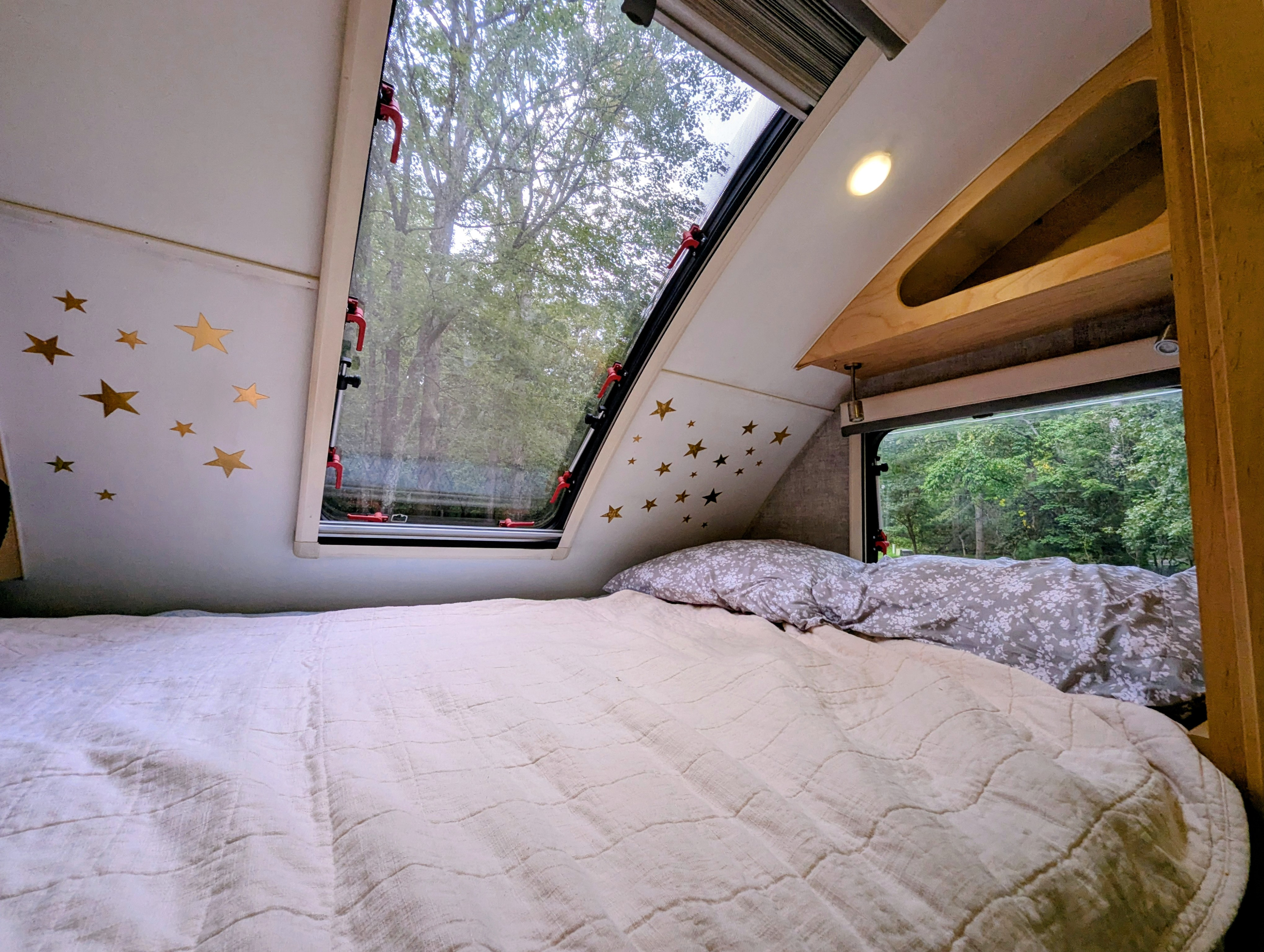 Cozy RV rental interior with a comfy bed, starry wall, and a large window overlooking lush green nature—ideal for camping.. Xtreme Outdoors Little Guy Max 2021