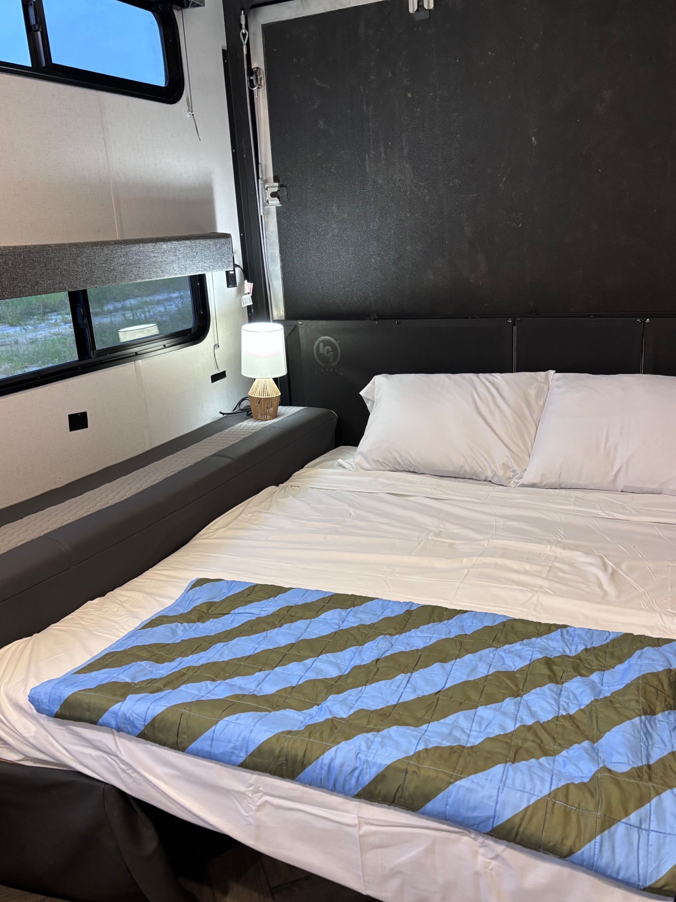 This RV rental's cozy bedroom features a bed with striped blanket, white pillows, and a lit bedside lamp.. Forest River Wildwood FSX 2021