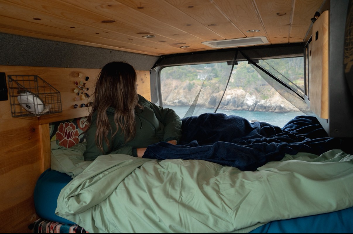 Relax in comfort: person viewing scenic coast from an RV rental bed. Perfect for a cozy camper van adventure.. Dodge Promaster 2500 2017
