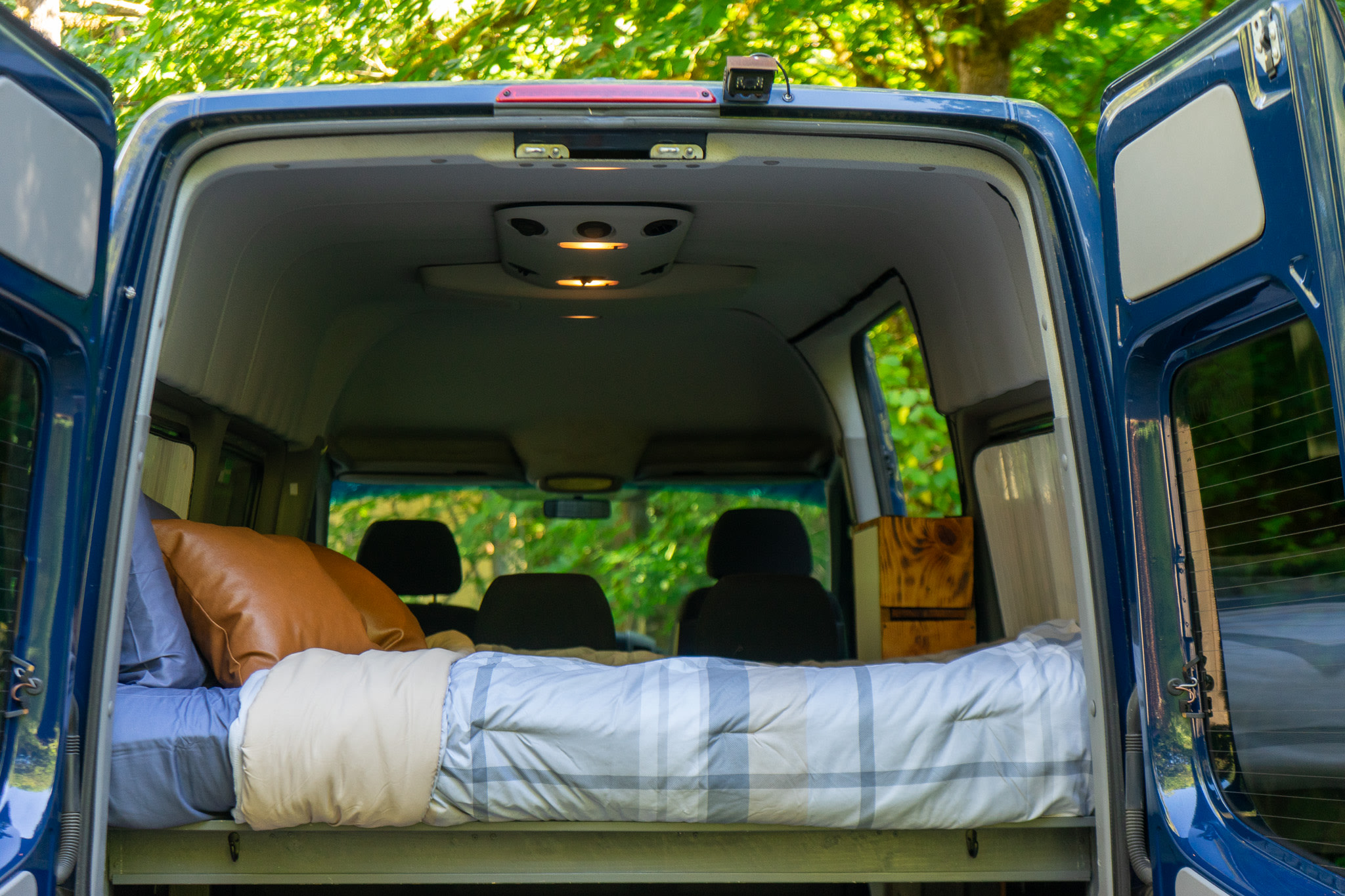 Open rear doors of a blue camper van revealing a comfy bed. Experience van life with this RV rental.. Mercedes-Benz Sprinter 2016