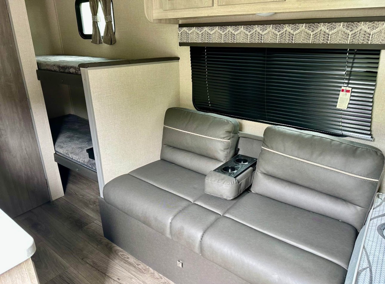 RV rental interior showing bunk beds, a gray sofa with cup holders, and a large window with blinds. Great for travel!. Coachmen Catalina 2023
