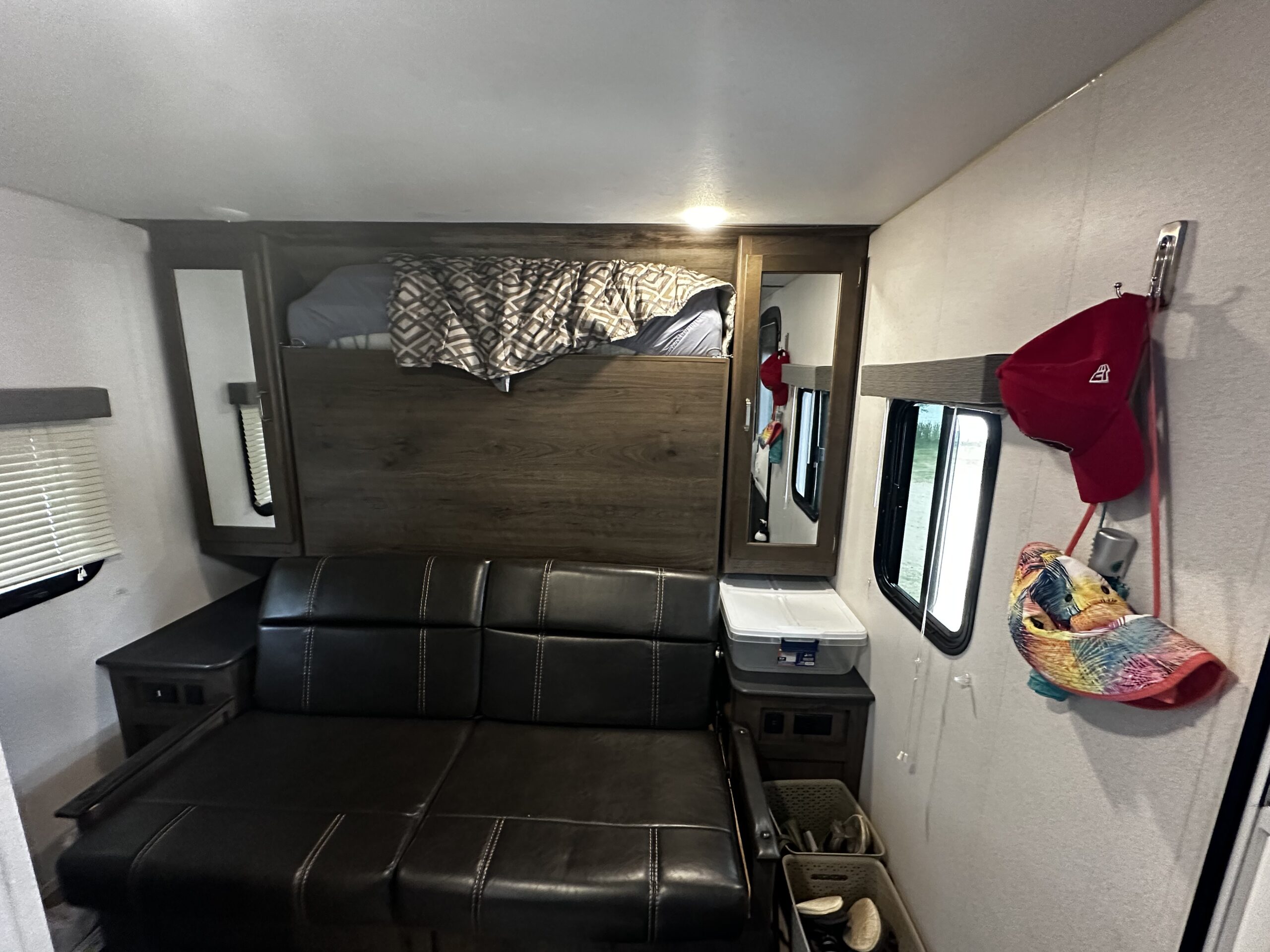 Inside an RV rental, a compact space features a bunk bed over a black leather sofa, with windows and storage bins.. KEYSTONE Passport 2019
