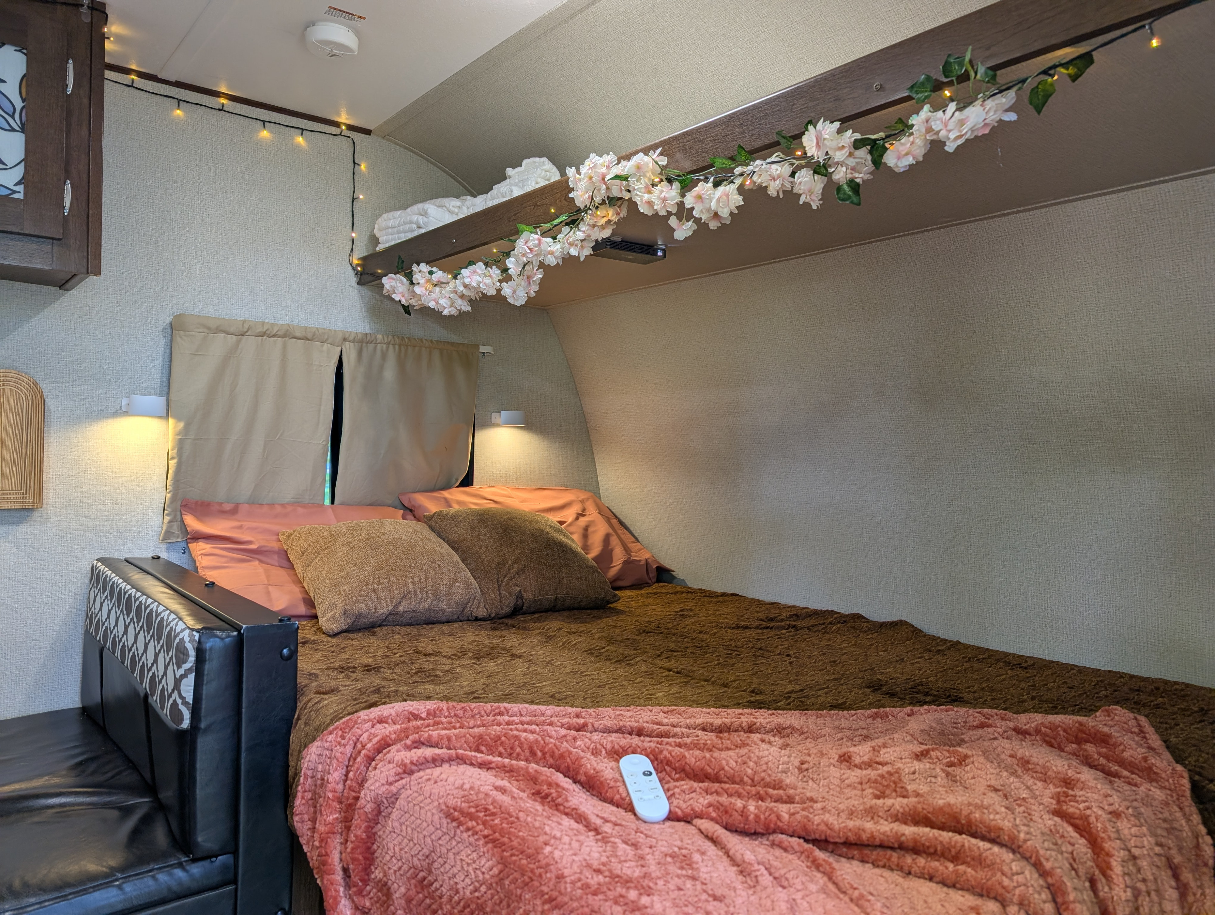 This RV rental offers a cozy bedroom with warm string lights, floral garland, and plush bedding for relaxing stays.. PTX PTX Trailer 2019