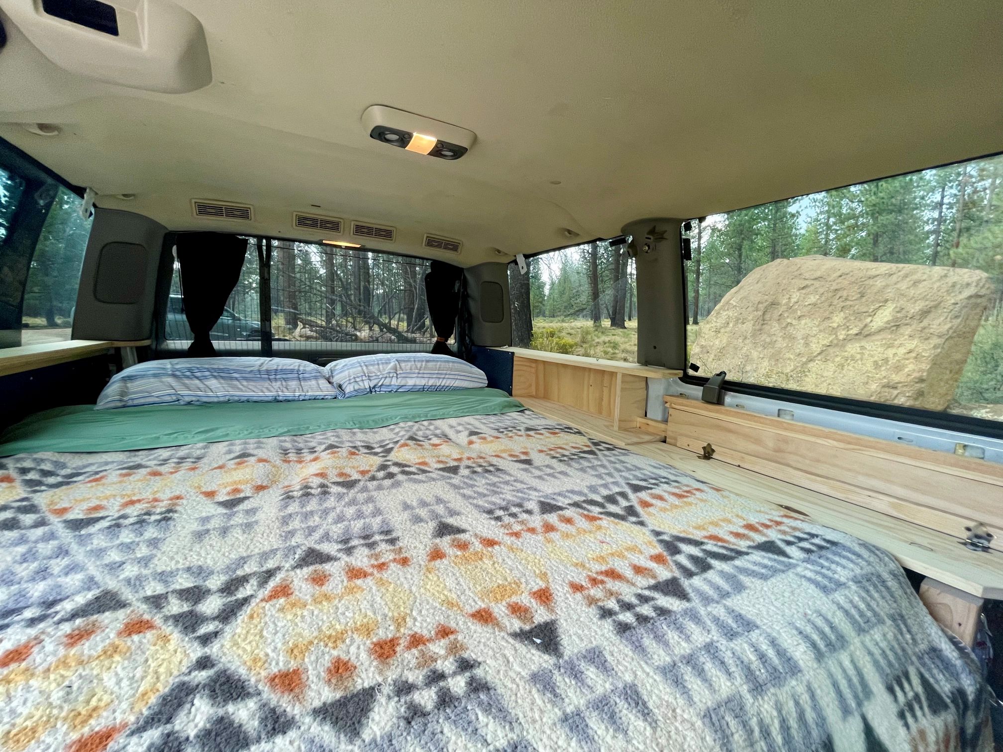 Cozy van bed with forest views, perfect for an RV rental. Designed for comfy, accessible camping trips.. Chevrolet Astro 2005