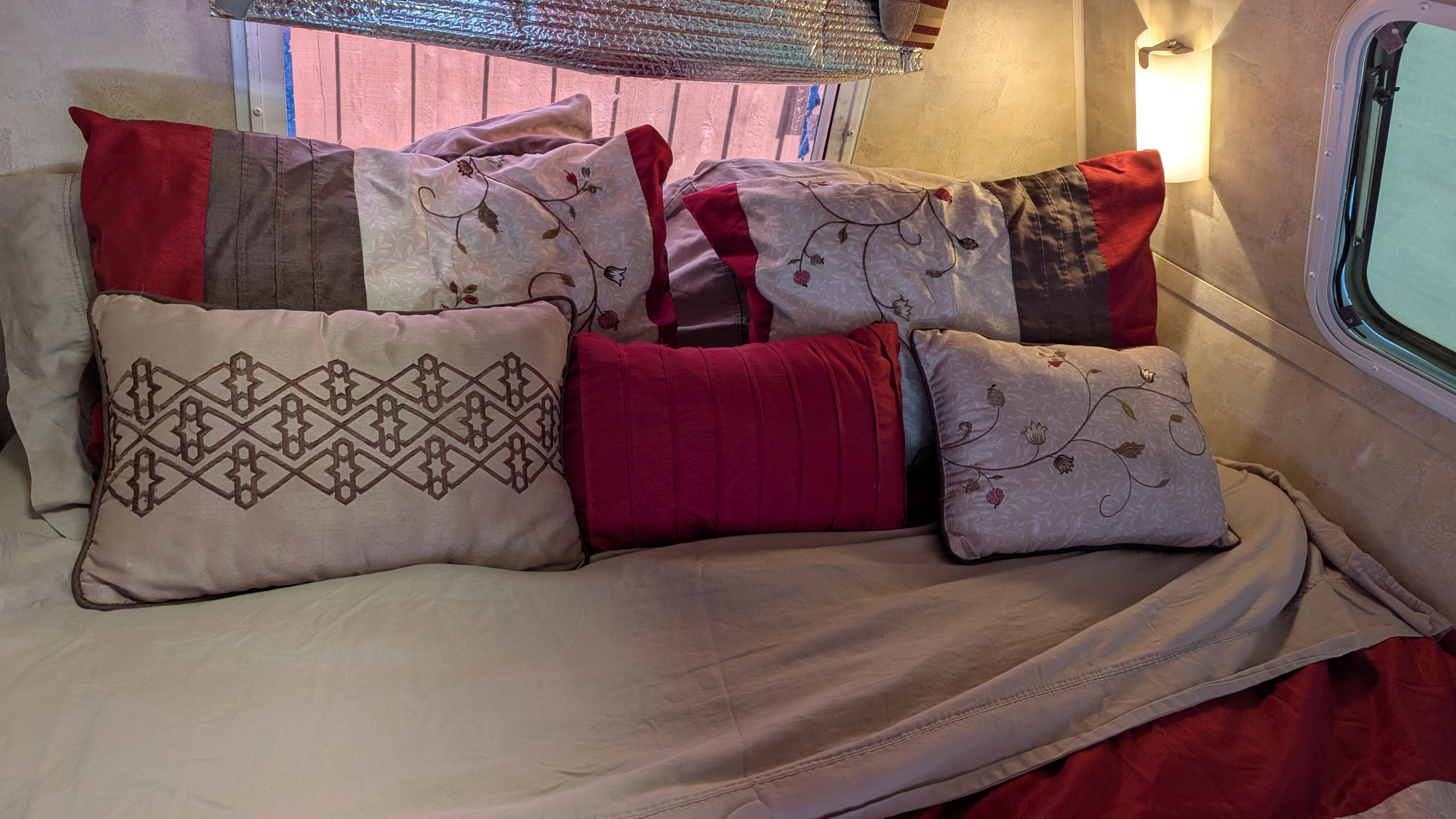 Inside an RV rental, a comfy bed with various red, grey, and cream decorative pillows offers a cozy retreat.. Eco Eco Trailer 2008
