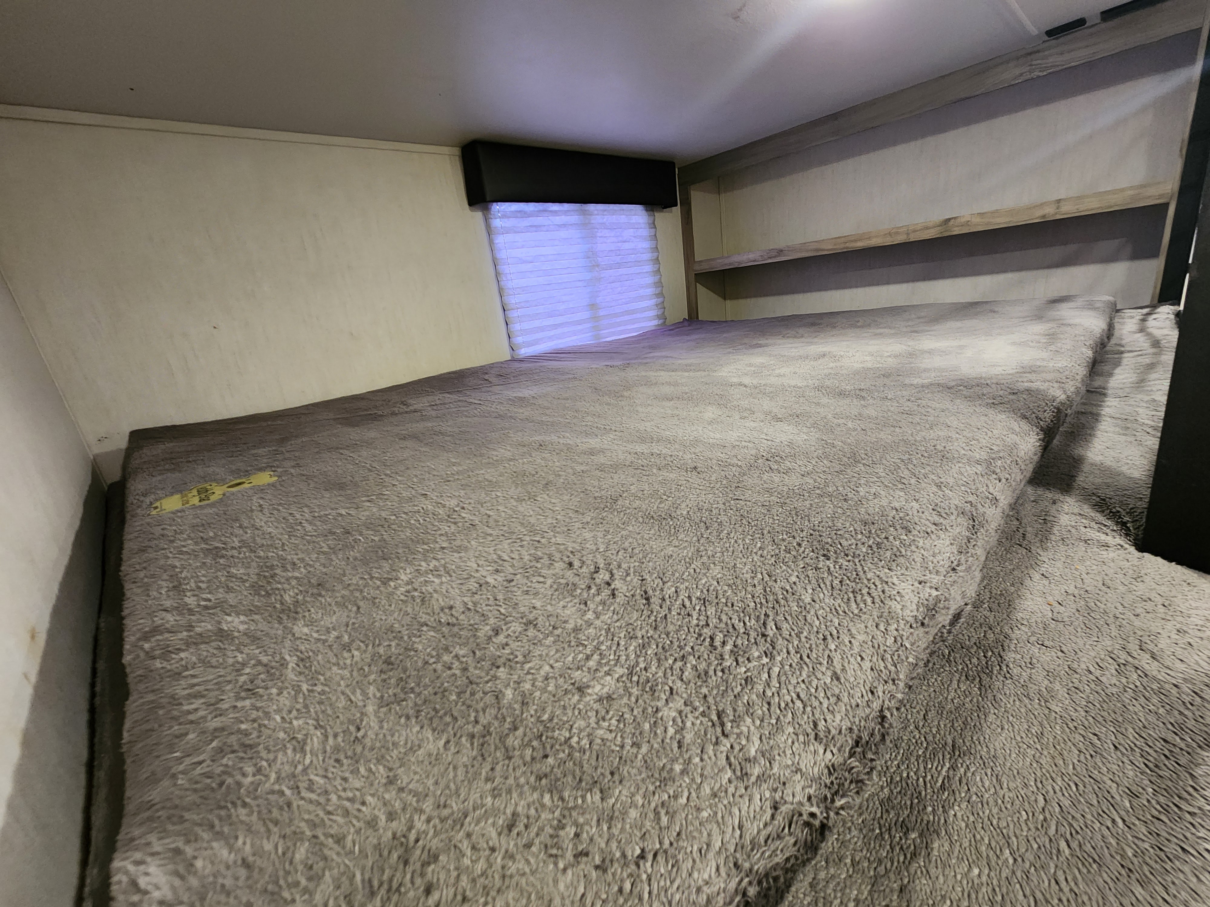 RV rental interior featuring a large, plush grey sleeping area with a window and wooden shelves for comfortable camper stays.. Forest River Cherokee Arctic Wolf 2022