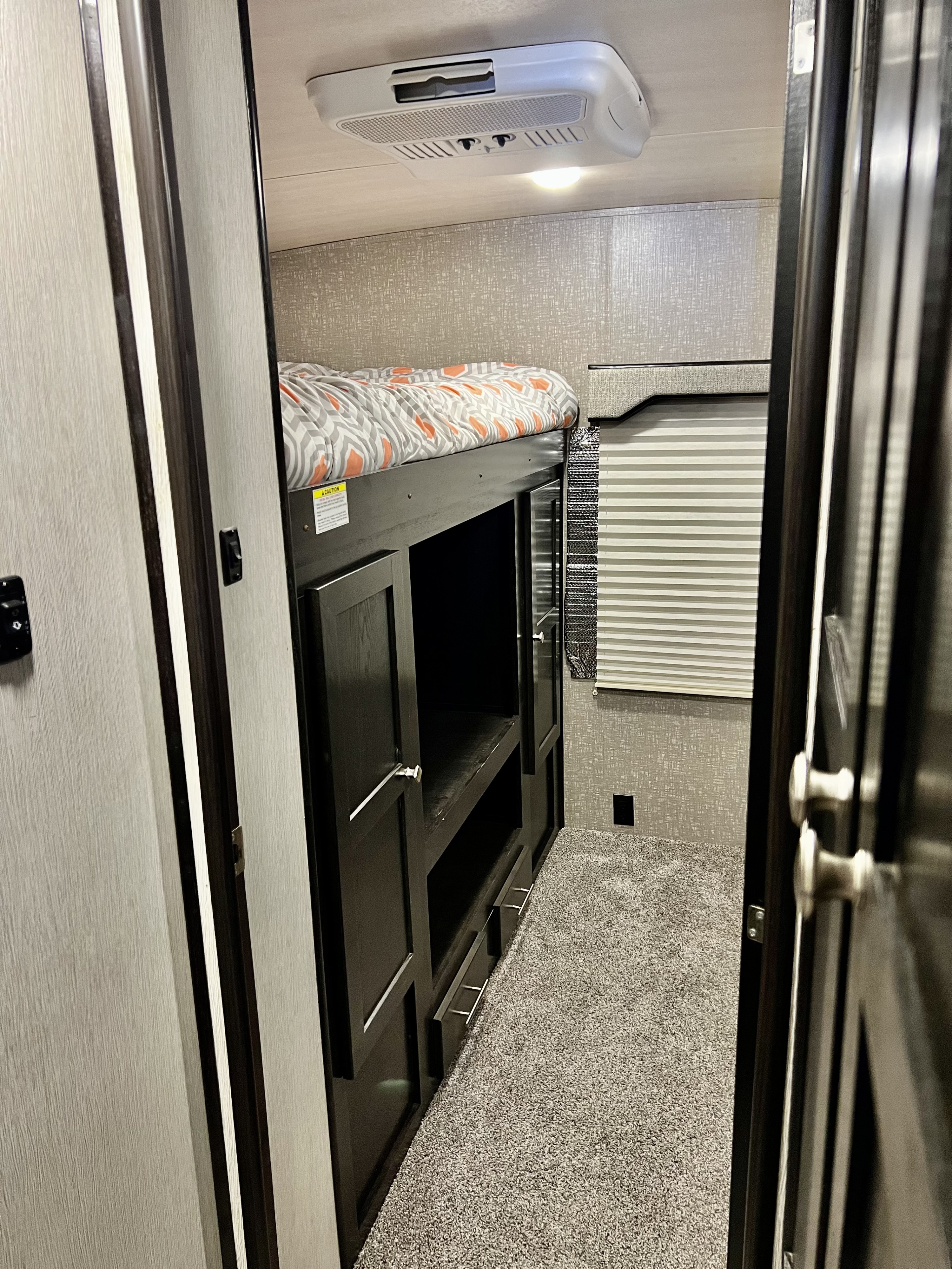 Cozy rv rental interior features bunk beds with a patterned comforter, overhead AC unit, and built-in storage.. Heartland RVs North Trail 2019