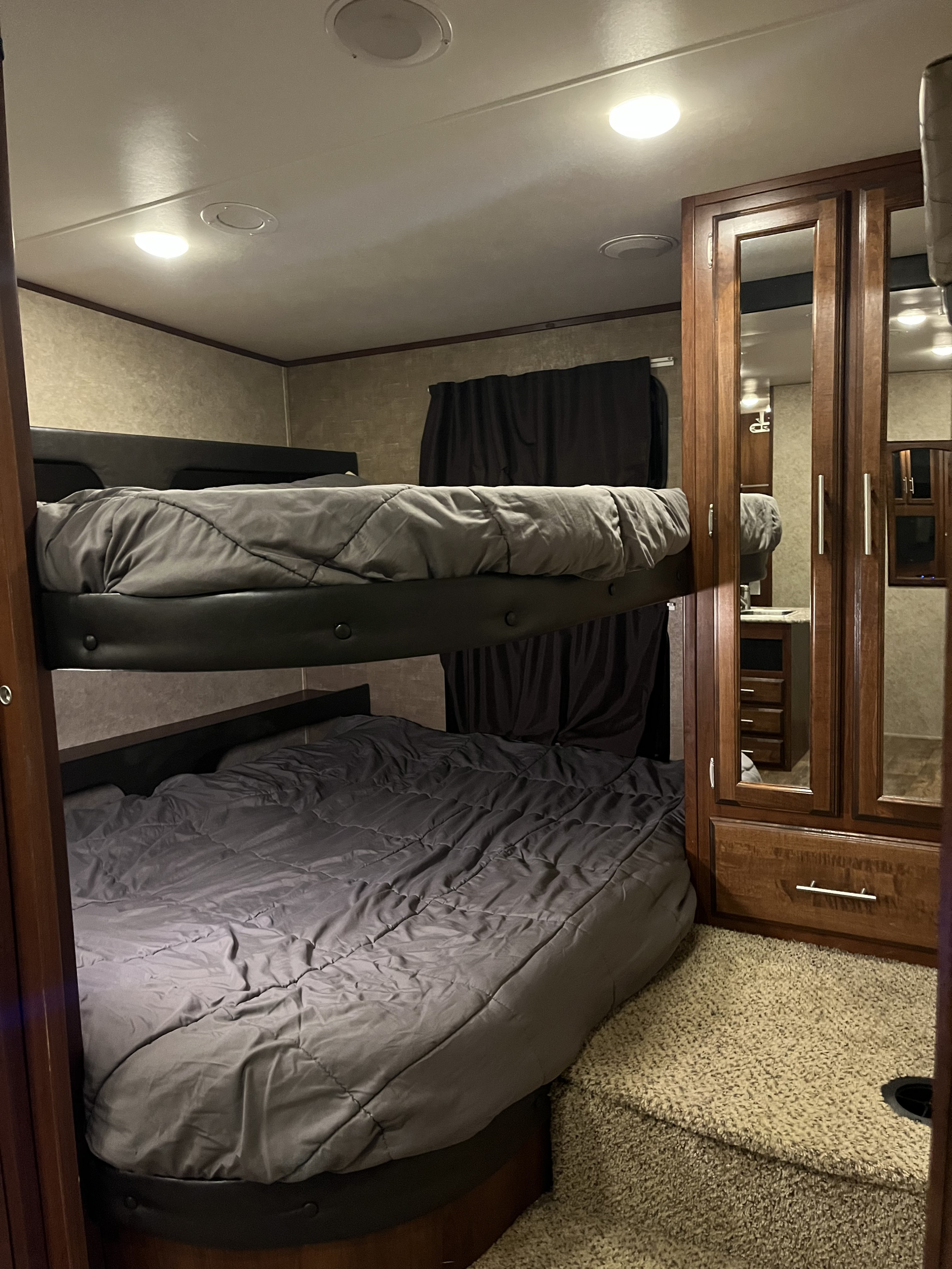 Inside a cozy RV rental: two bunk beds with grey bedding, a mirrored wardrobe, and carpeted floor offer compact sleeping.. Jayco Eagle HT 2017
