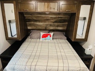 Step into comfort with this RV rental bedroom, featuring a cozy bed, wooden cabinets, and mirrored storage for your travels.. Keystone Passport 2021