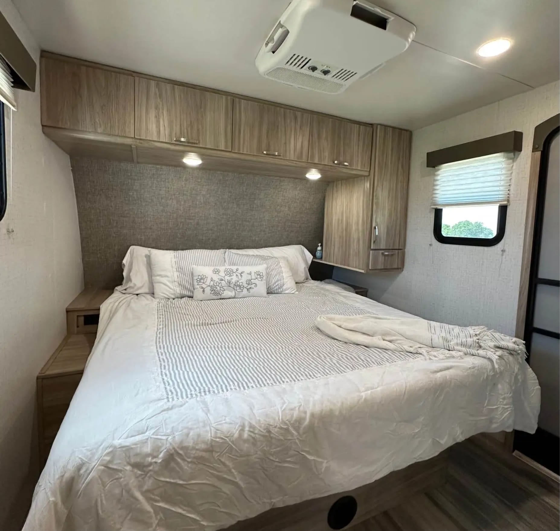 Experience comfort in this RV rental bedroom: cozy bed, overhead cabinets, textured headboard, and a window for natural light.. Minnie Minnie Trailer 2022