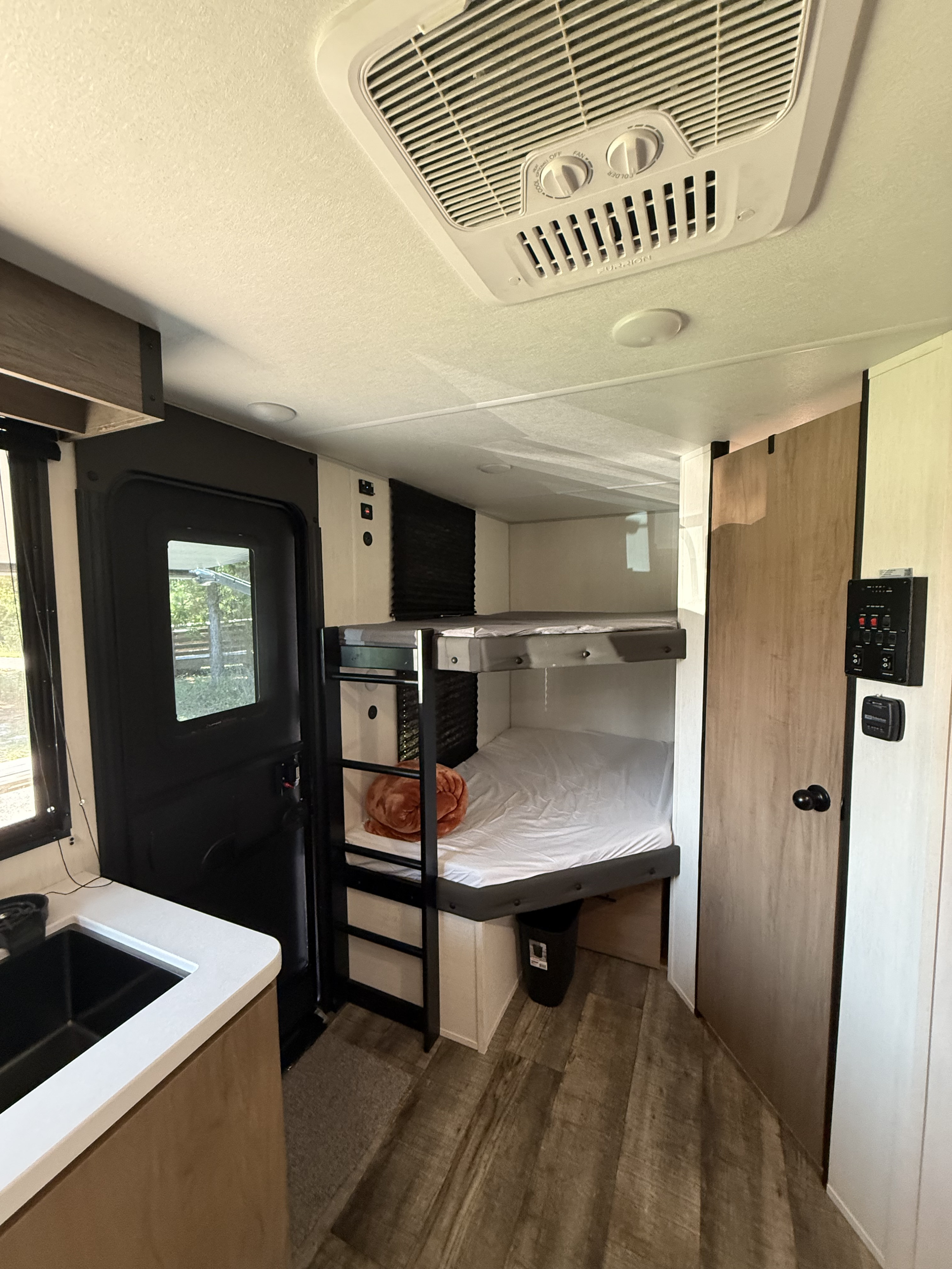 This RV rental interior shows bunk beds, a kitchen counter with sink, entrance door, and ceiling AC unit.. Forest River Campsite Reserve LS17 2025