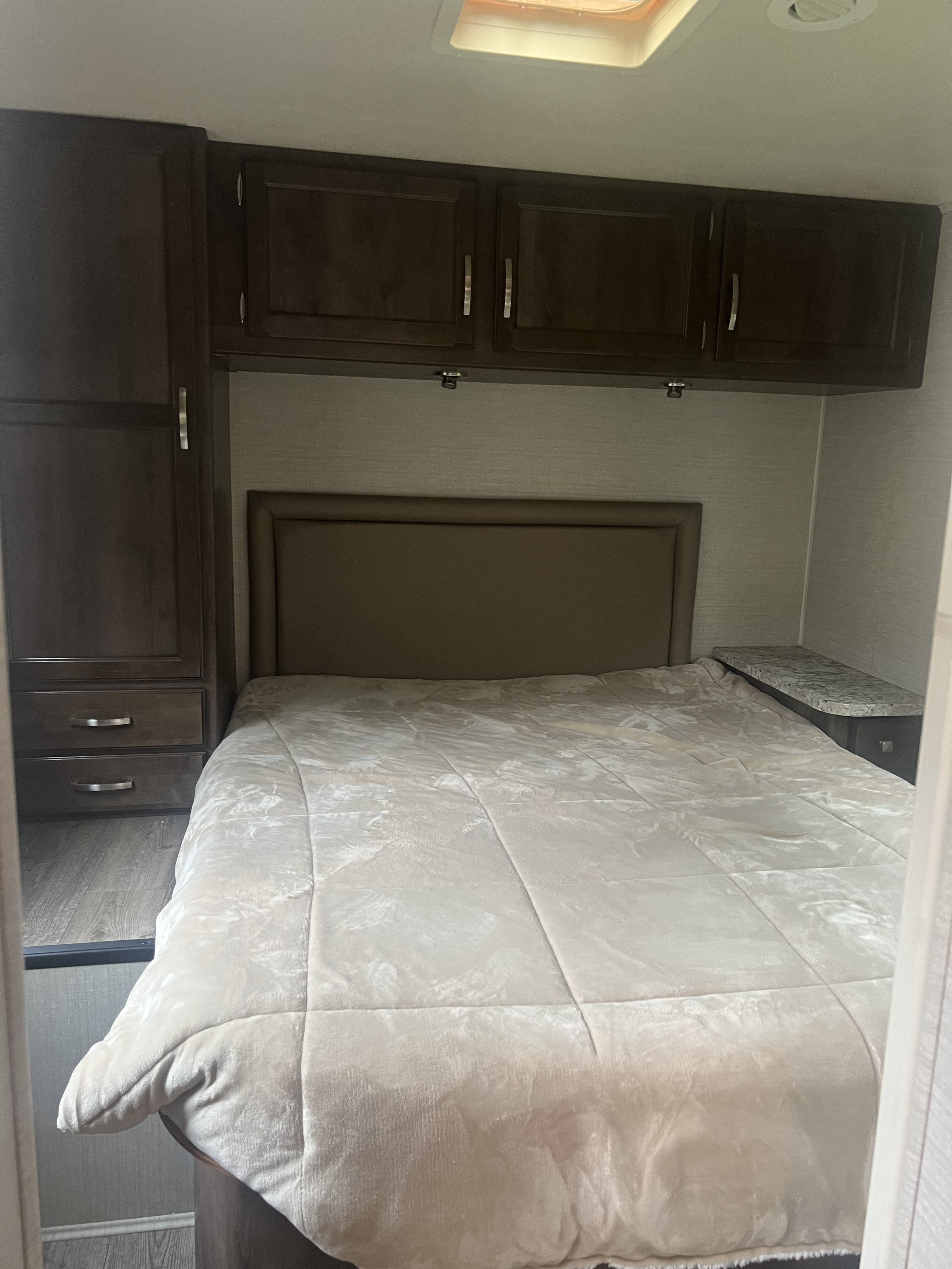 Compact RV rental bedroom featuring a bed with a light comforter, dark overhead storage cabinets, and a side dresser.. Jayco Greyhawk 2018
