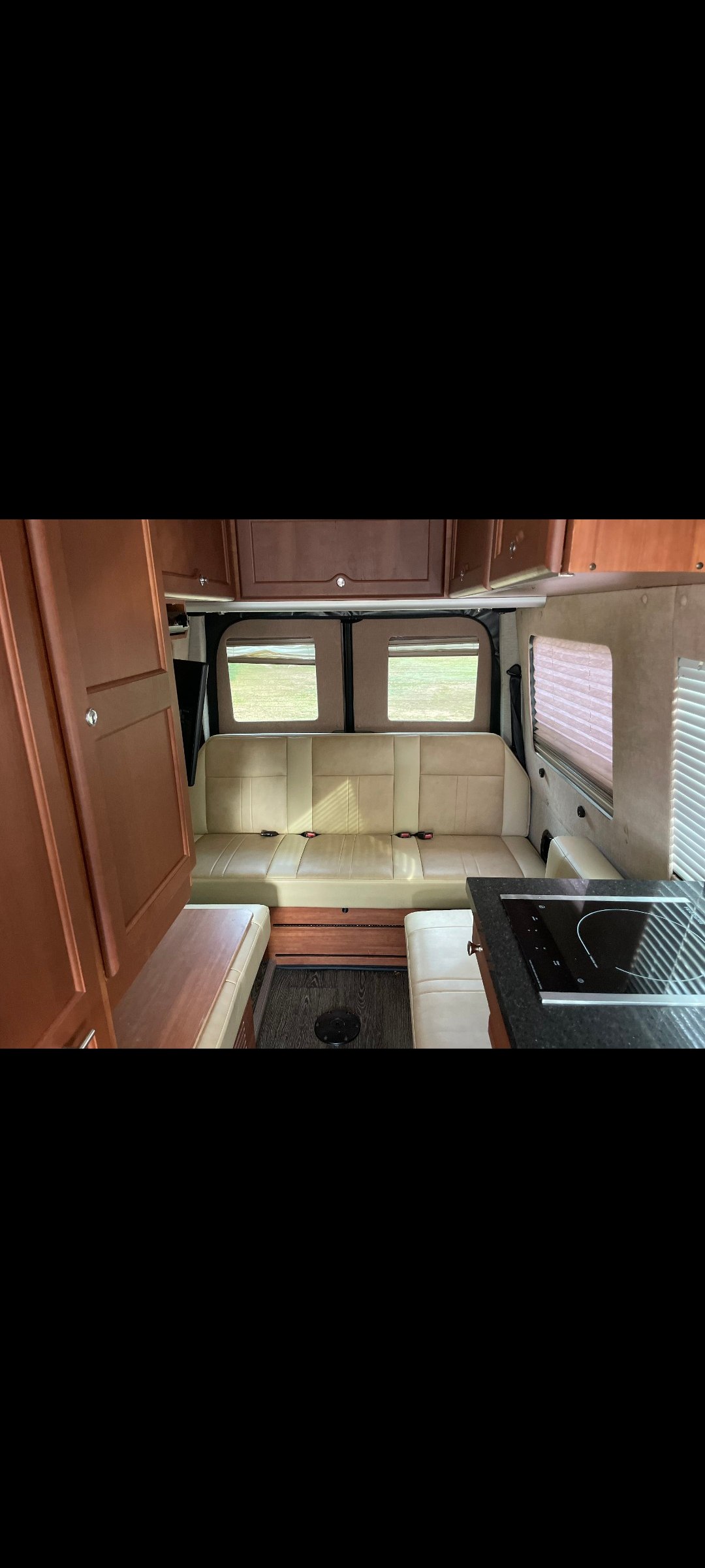 Inside this modern RV rental: light bench seating, wood cabinetry, and a compact kitchen with a cooktop.. Roadtrek Roadtrek Class B 2016