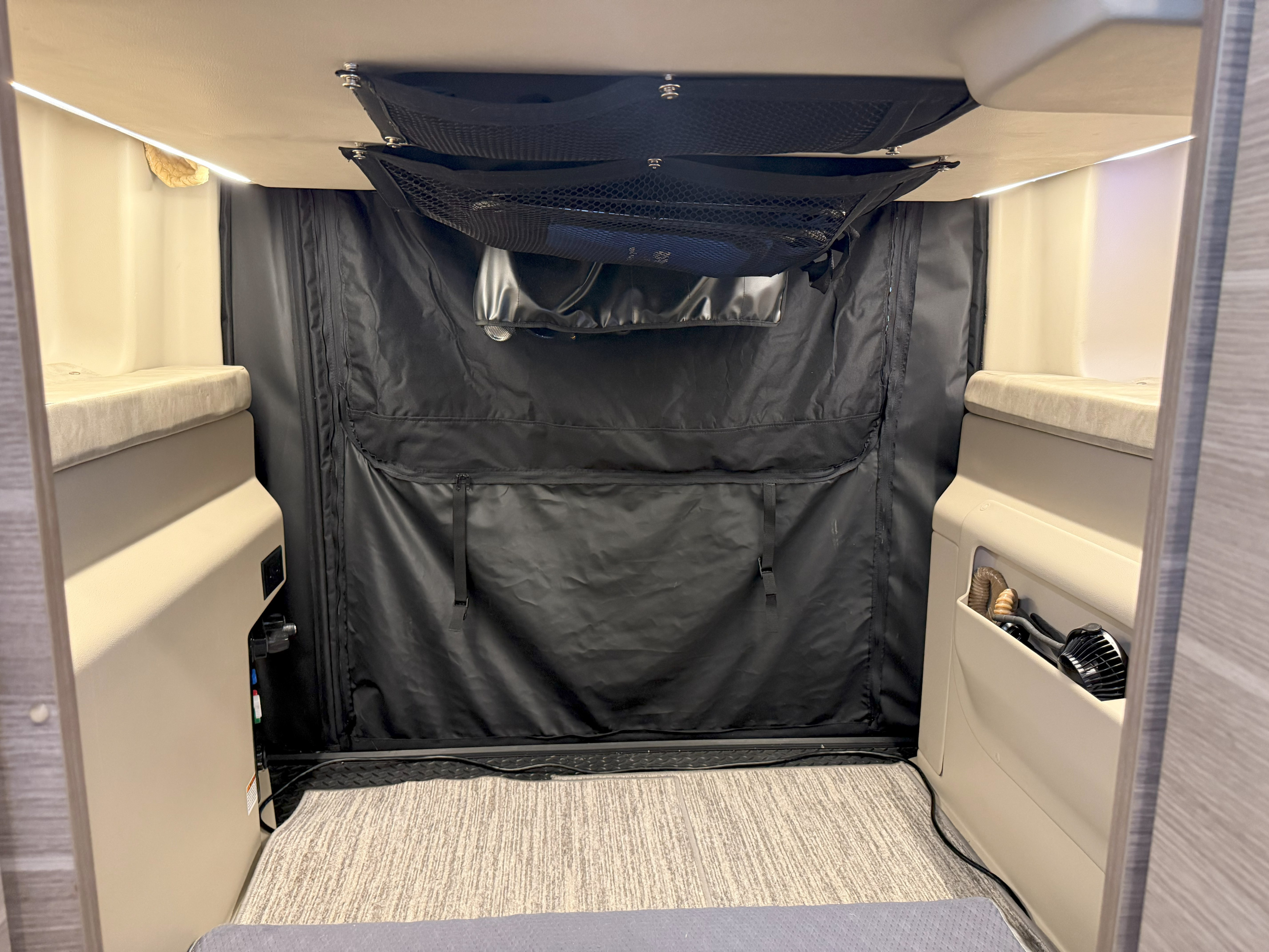 RV rental interior showing compact bunk beds, overhead mesh storage, and a black fabric divider for an organized space.. Entegra Coach Launch 2023