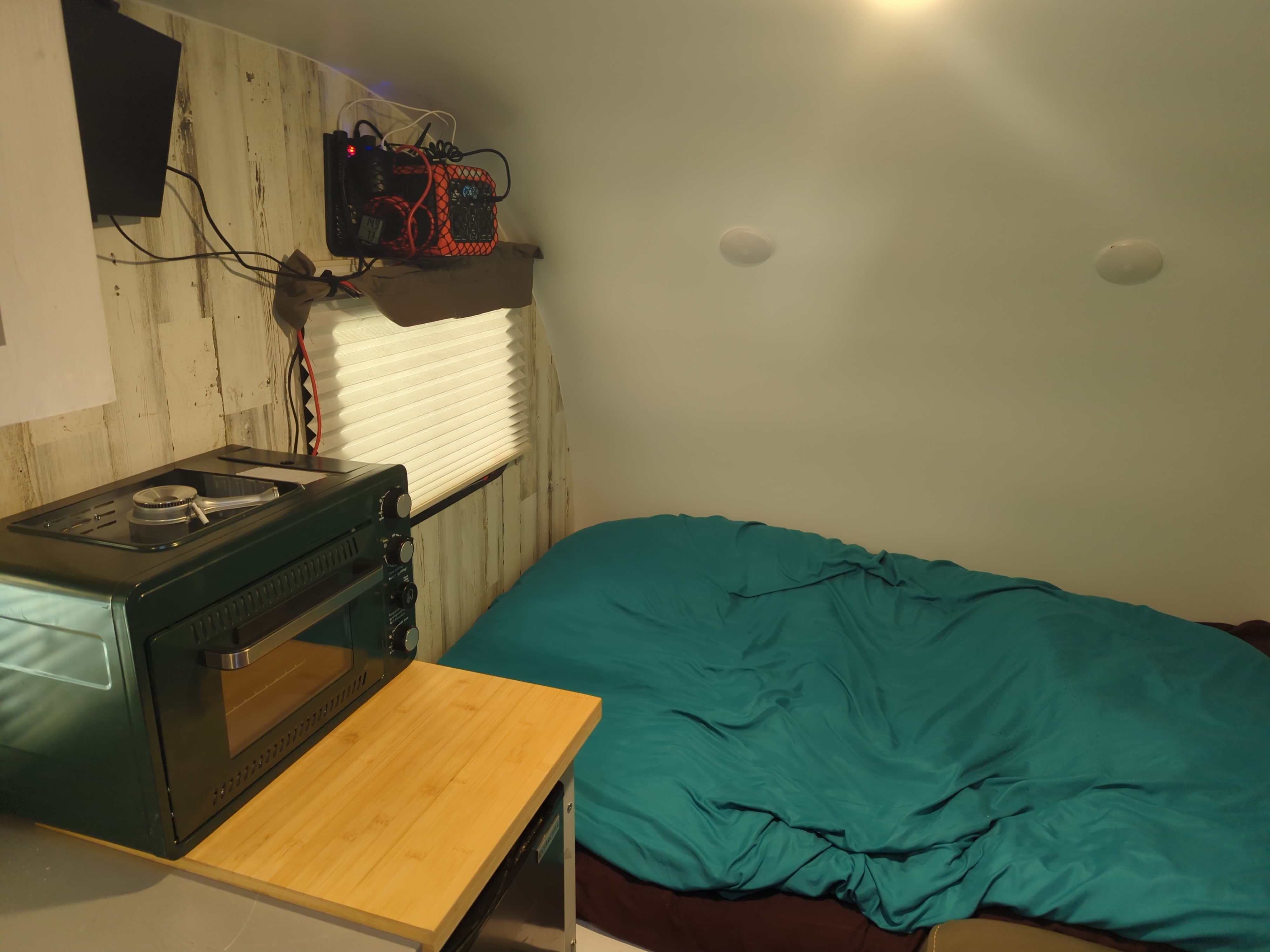 Compact RV rental interior featuring a bed, small kitchenette with oven, and wall-mounted electronics, perfect for travel.. Travel Lite Rove Lite 2023