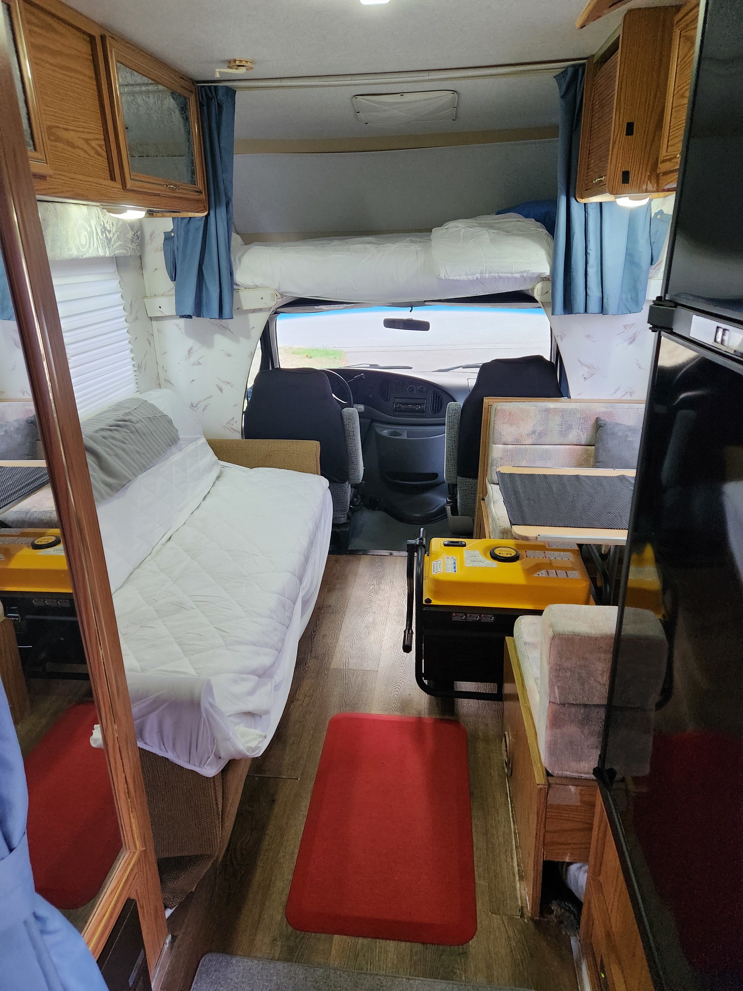 An rv rental's cozy interior: front cockpit, overhead bunk, main bed, and living area with a generator.. Ford Winnebago Itasca 1997