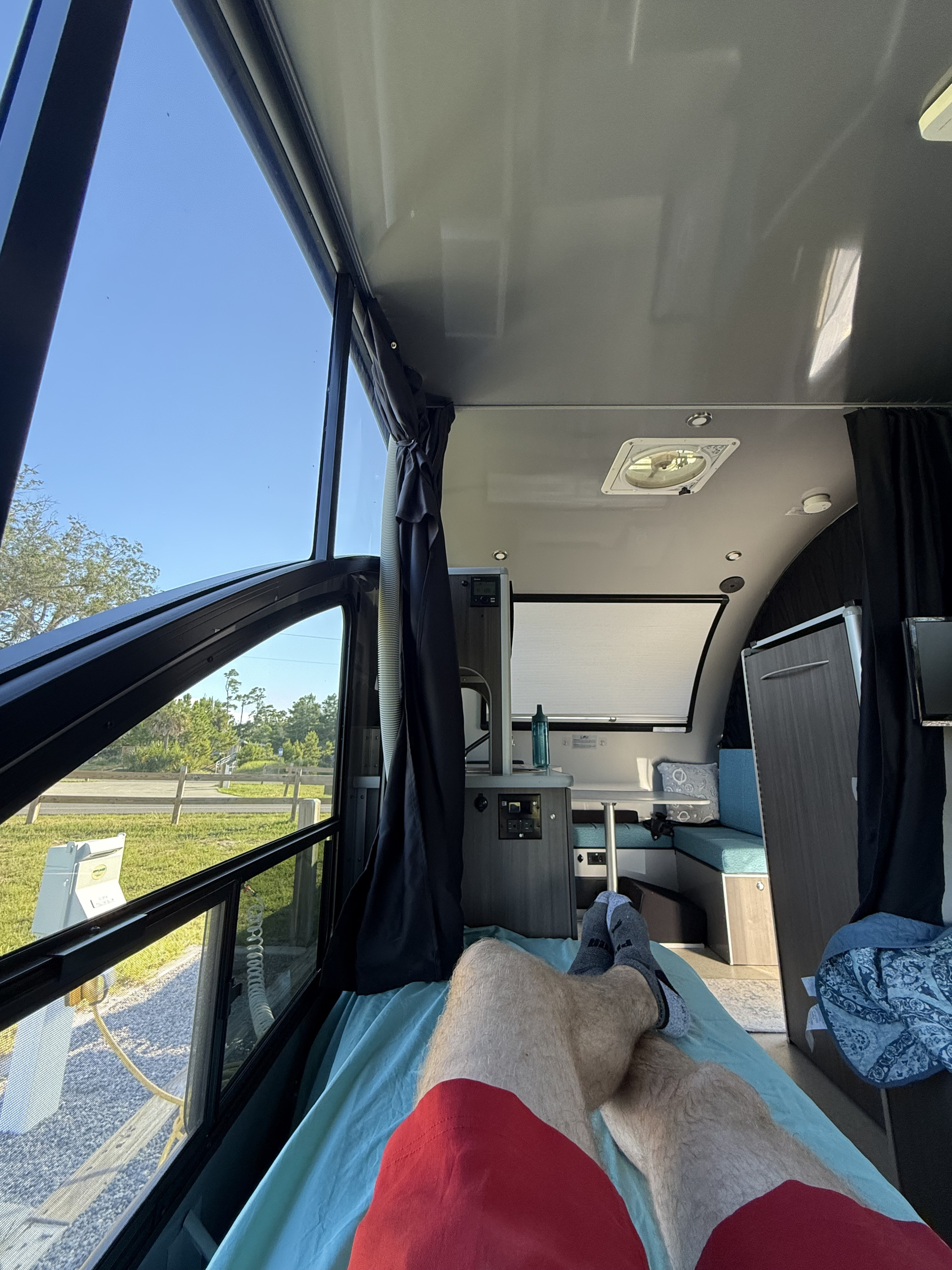 Relaxing inside an RV rental, showing a person's legs, a large window view of a campsite, and the cozy interior.. Alto Safari Condo R1713 2024