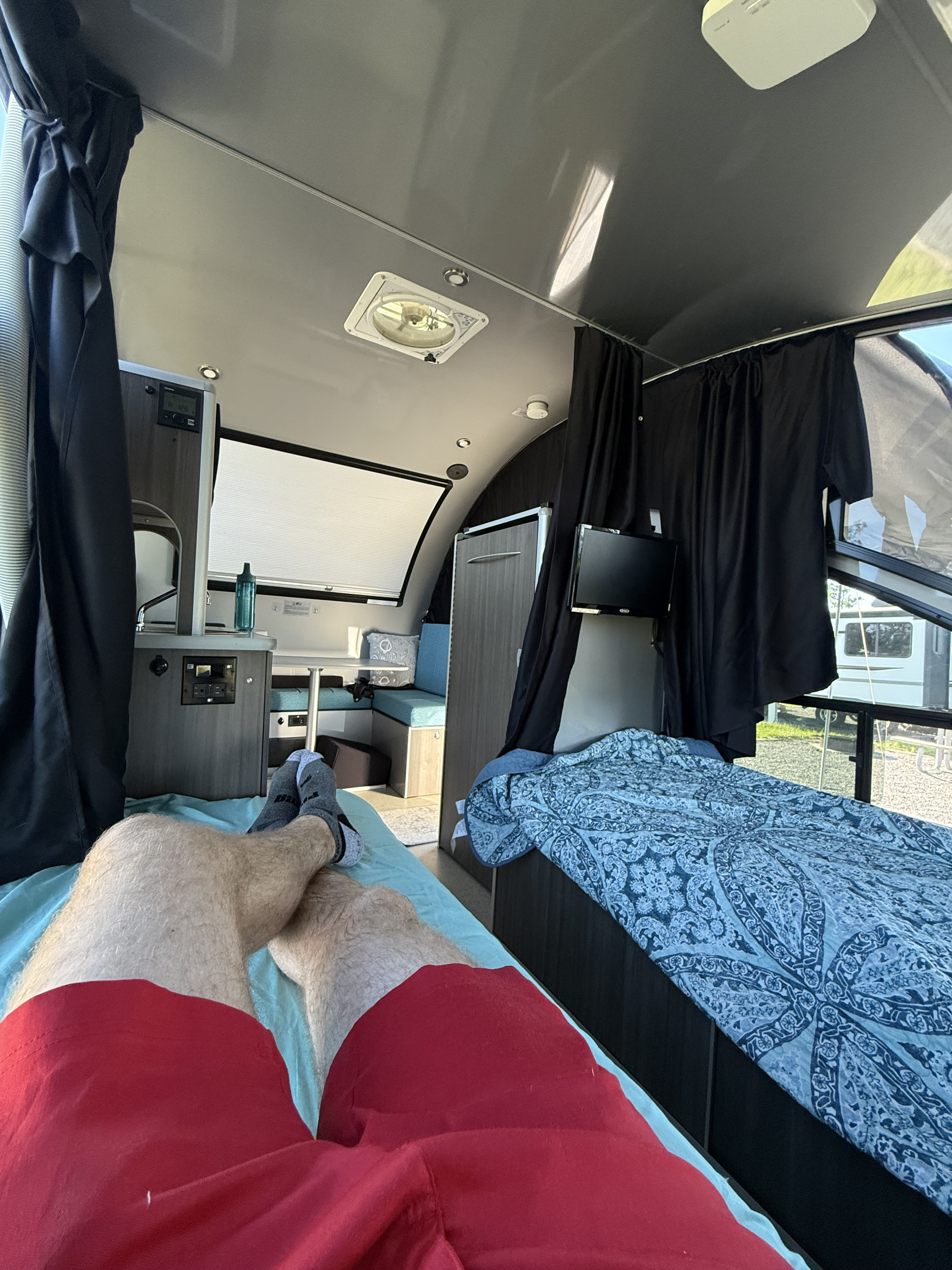 Relaxing inside a modern RV rental: view of legs on bed, with dinette, another bed, & TV. Cozy travel setup.. Alto Safari Condo R1713 2024
