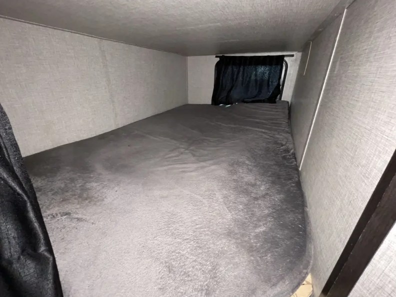 This RV rental features a cozy bunk bed with grey bedding and a window curtain, providing a compact sleeping area.. Jayco Jay Flight 2022