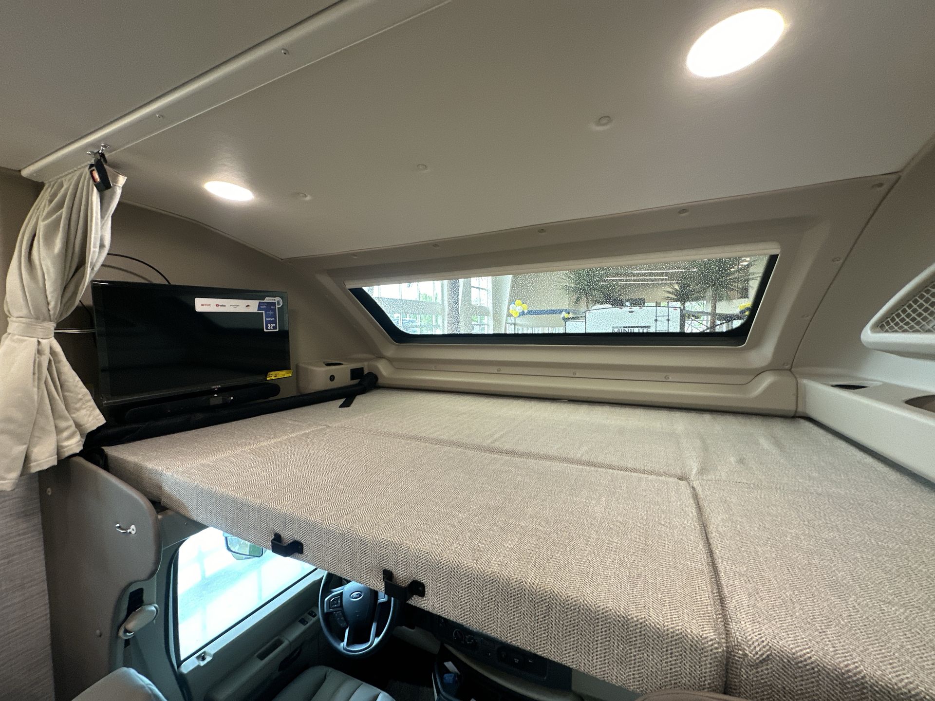 Explore this RV rental's cozy cab-over bunk interior, featuring a comfortable mattress, TV, and bright window.. Jayco Greyhawk 31F 2025