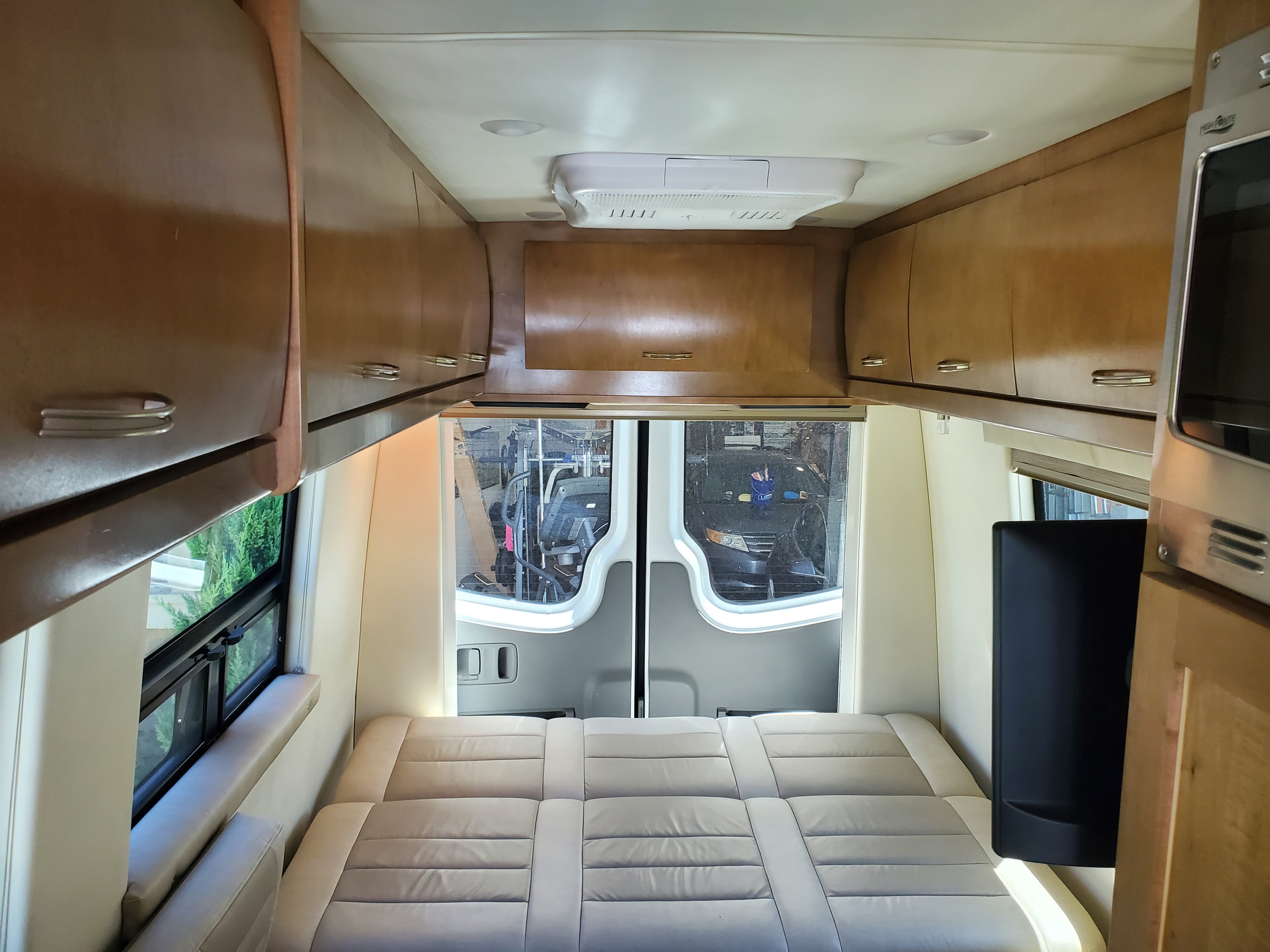 RV rental interior: a plush bed at the rear, flanked by windows, with overhead wood cabinets, a TV, and microwave.. Coachmen Galleria 2019