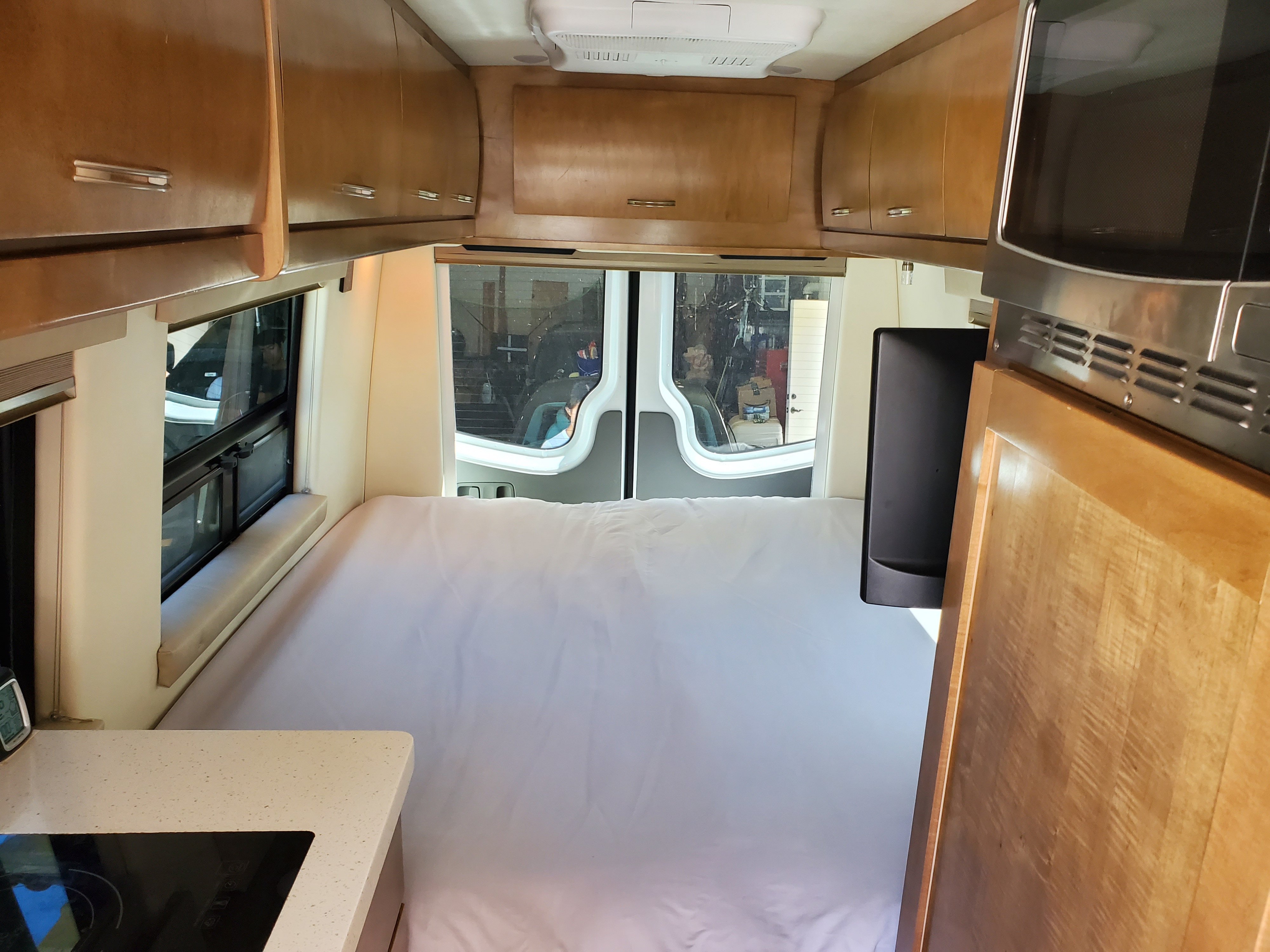 View inside an RV rental van: bed, kitchen counter, and wooden overhead storage for travel.. Coachmen Galleria 2019