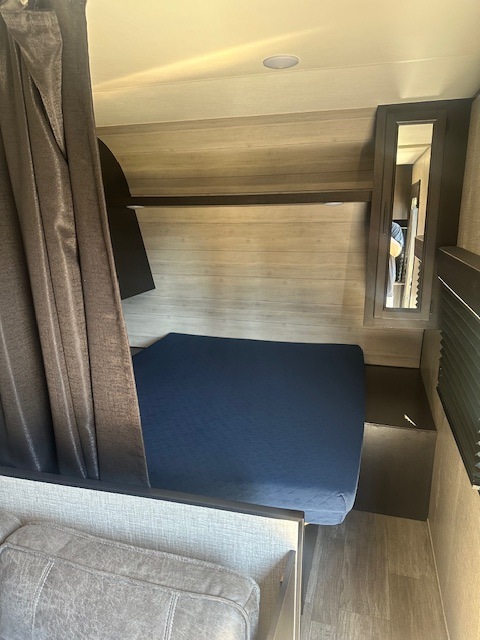 Cozy RV rental bunk bed setup: blue mattress, privacy curtain, shelf, and mirror for comfort and convenience.. Jayco Jay Flight SLX 2022
