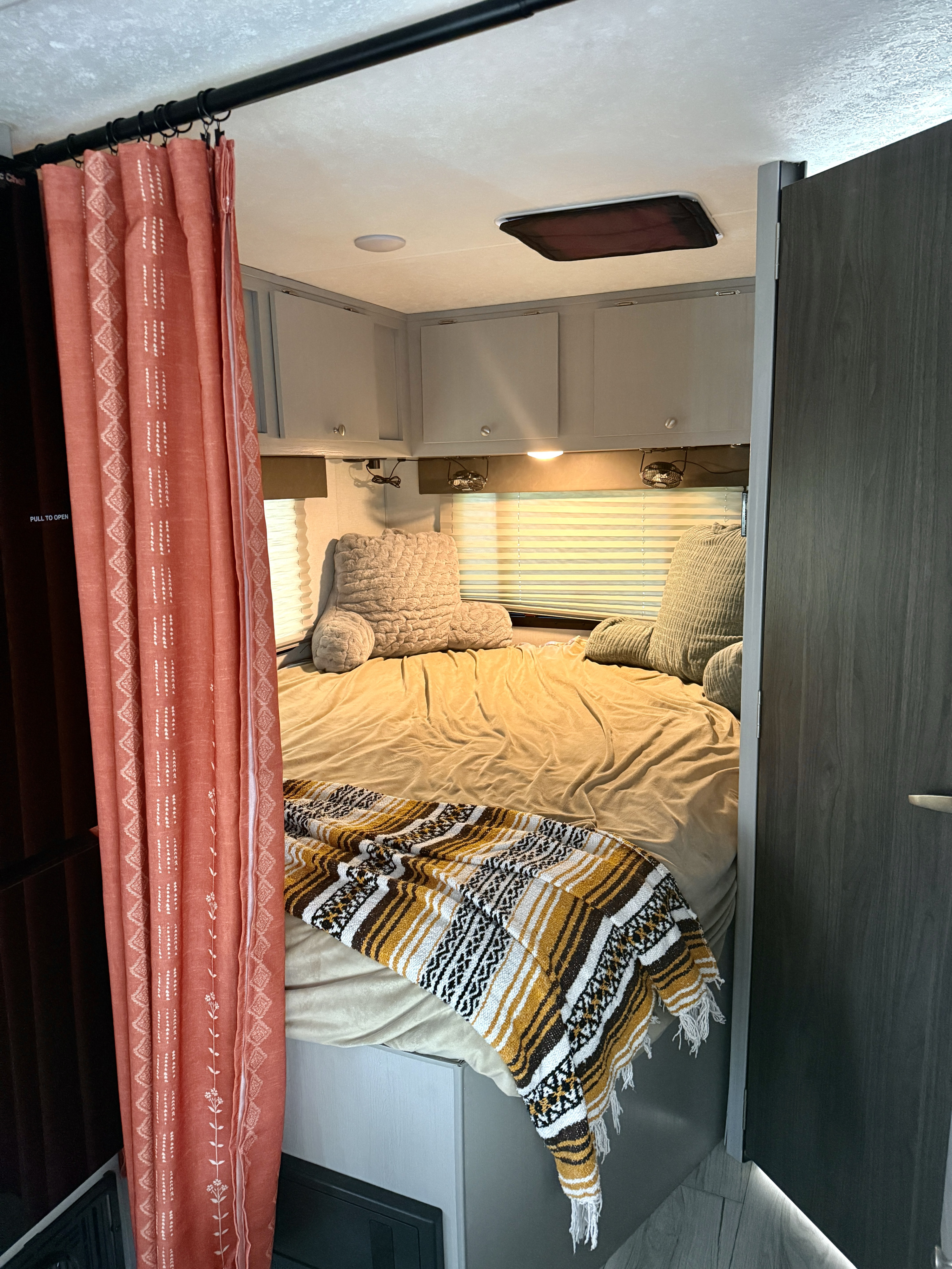 Cozy RV rental bedroom with a bed, patterned throw, light grey overhead cabinets, and a coral curtain. Perfect for travel.. Forest River Coachman Freelander 21QSS 2025