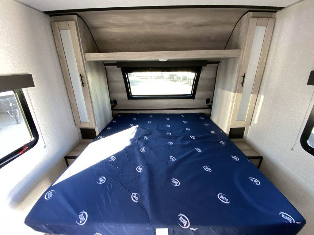 This RV rental's bedroom interior features a blue-covered bed, side windows, and overhead storage, designed for compact travel comfort.. Connect Connect Trailer 2021