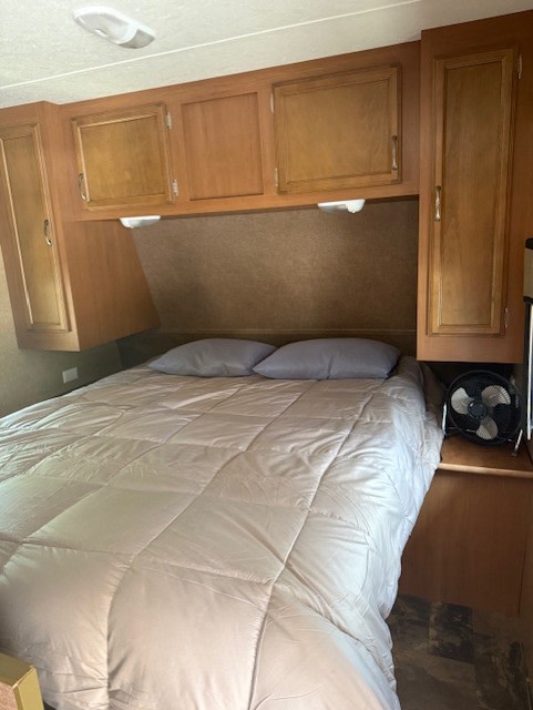 This RV rental's cozy bedroom features a comfortable bed, ample overhead storage cabinets, and a small fan.. StarCraft Autumn Ridge 2013