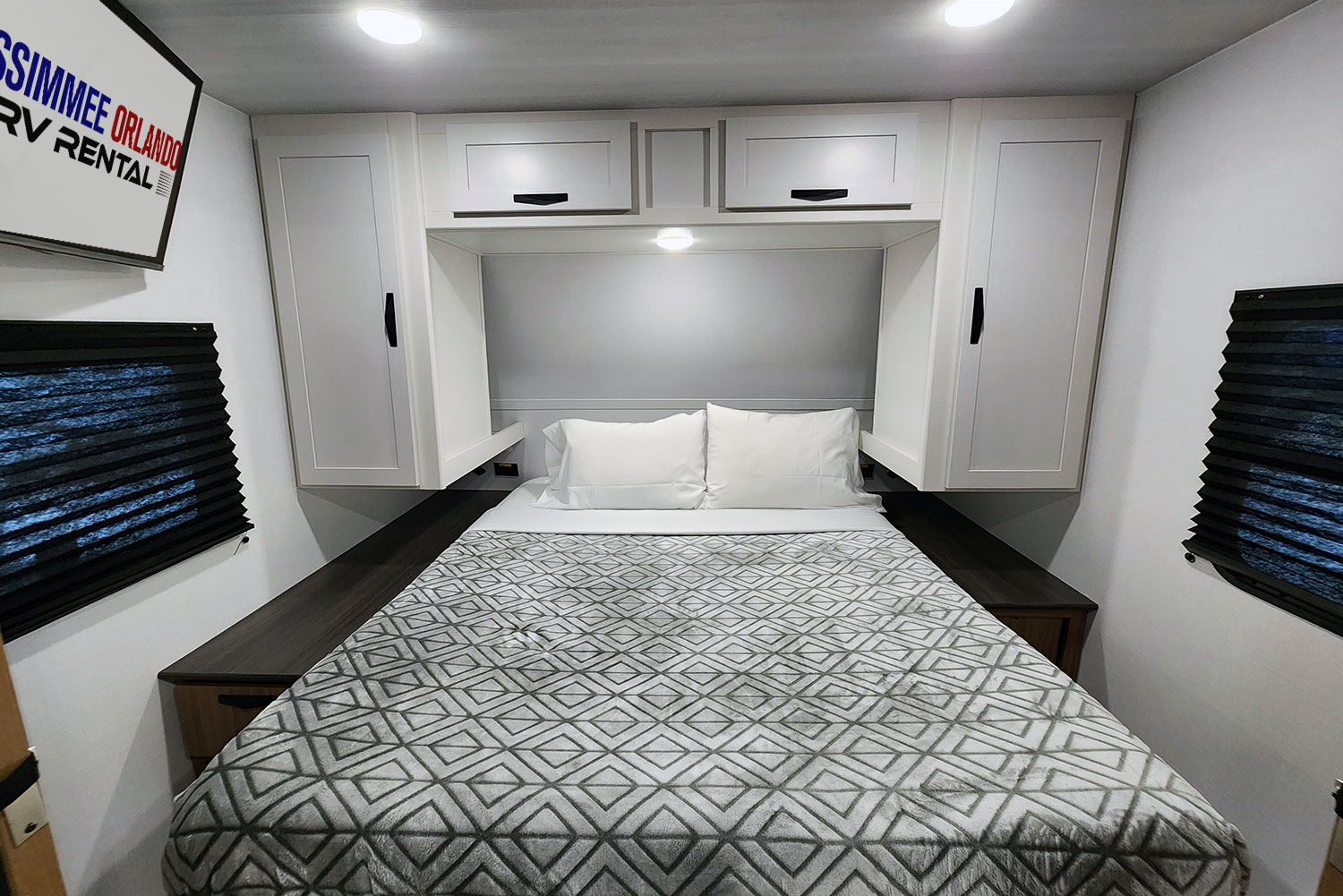 Modern RV rental bedroom with a comfortable bed, overhead cabinets, and side shelving.. Keystone Passport 2025