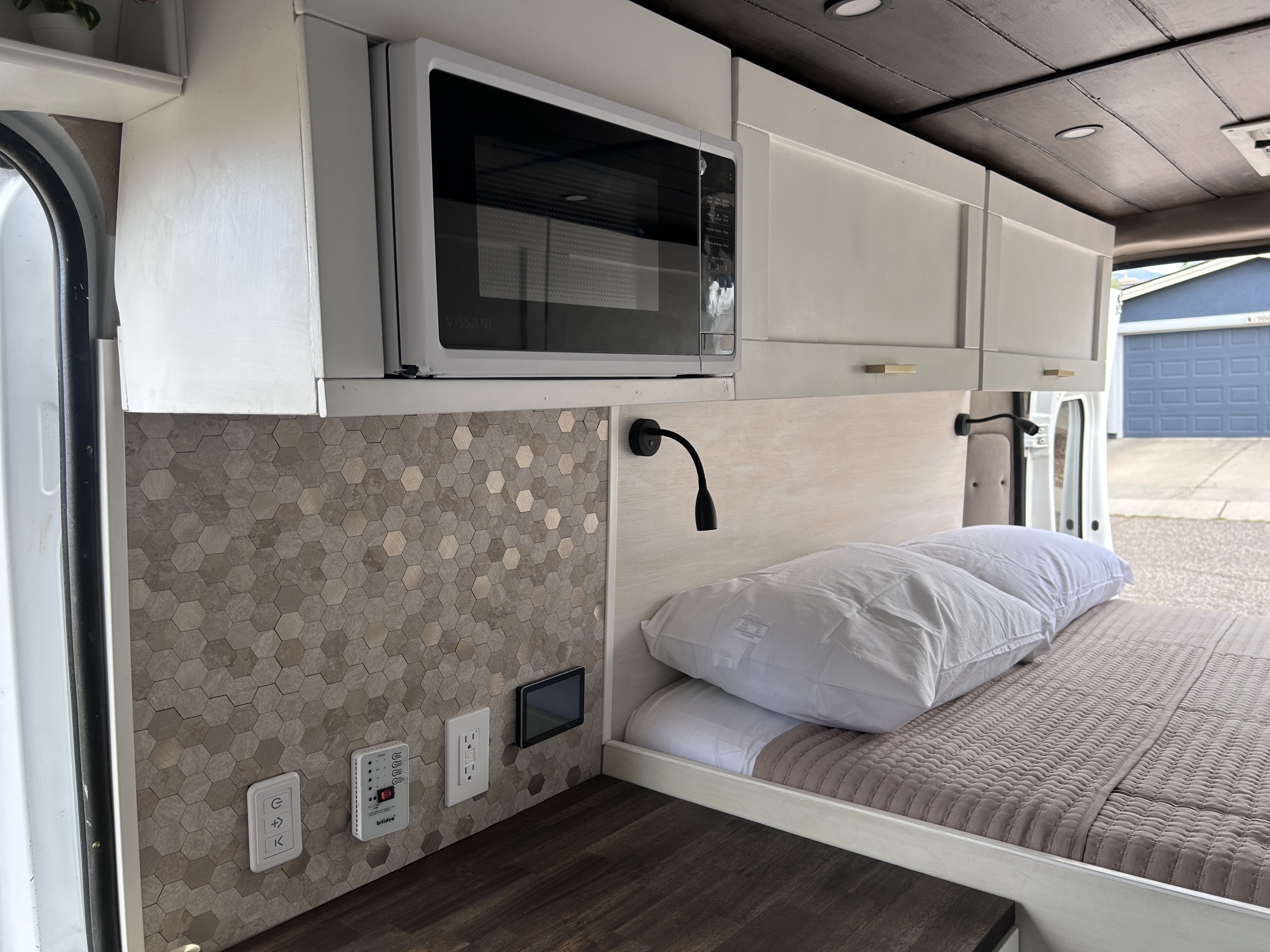 Sleek RV rental interior showcases a microwave, overhead cabinets, hexagon tile backsplash, and a cozy bed area.. Ram Promaster 2500 2022