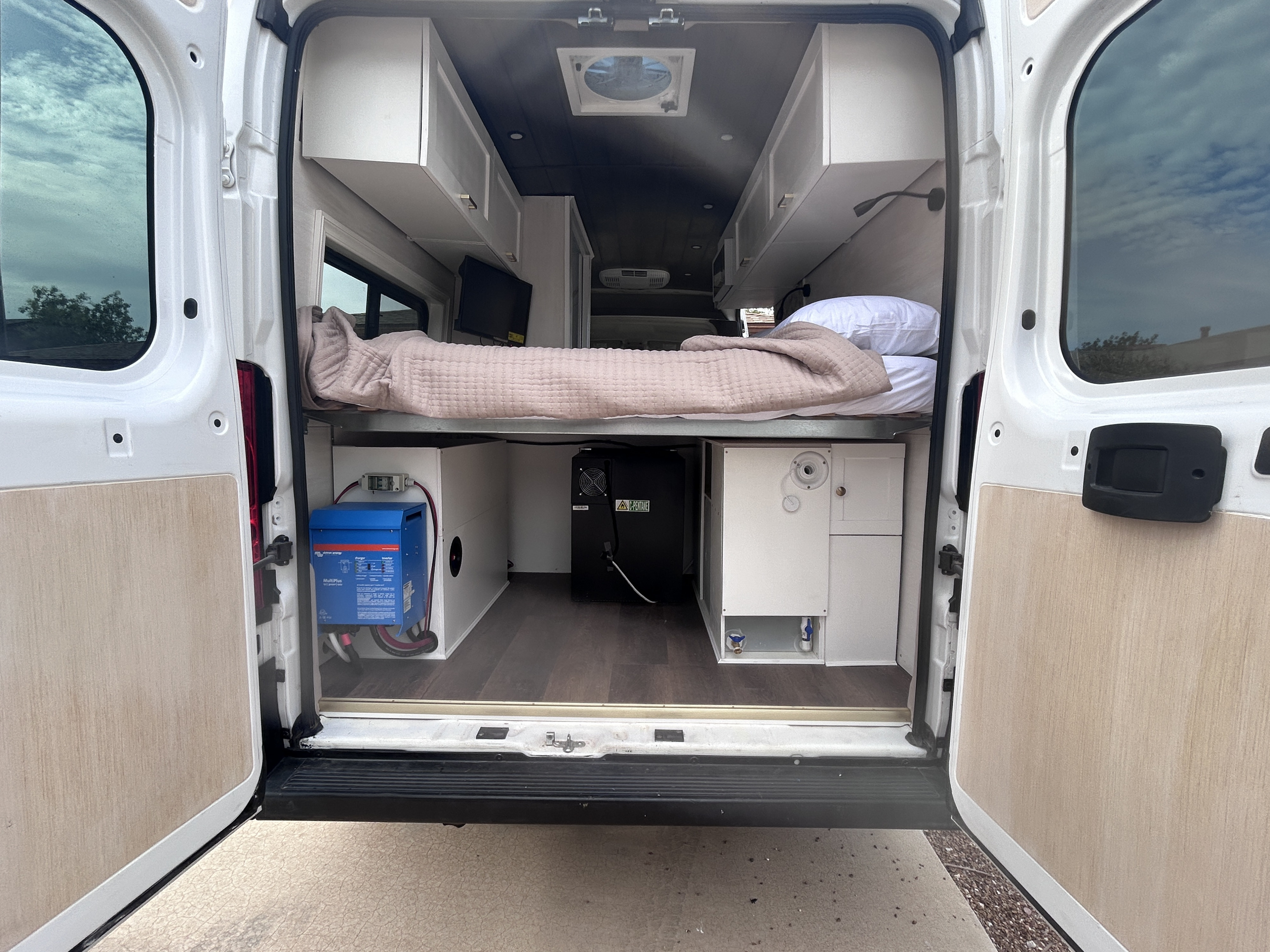 Rear view of an RV rental: modern camper van interior with bed, storage, power, and water systems clearly visible.. Ram Promaster 2500 2022