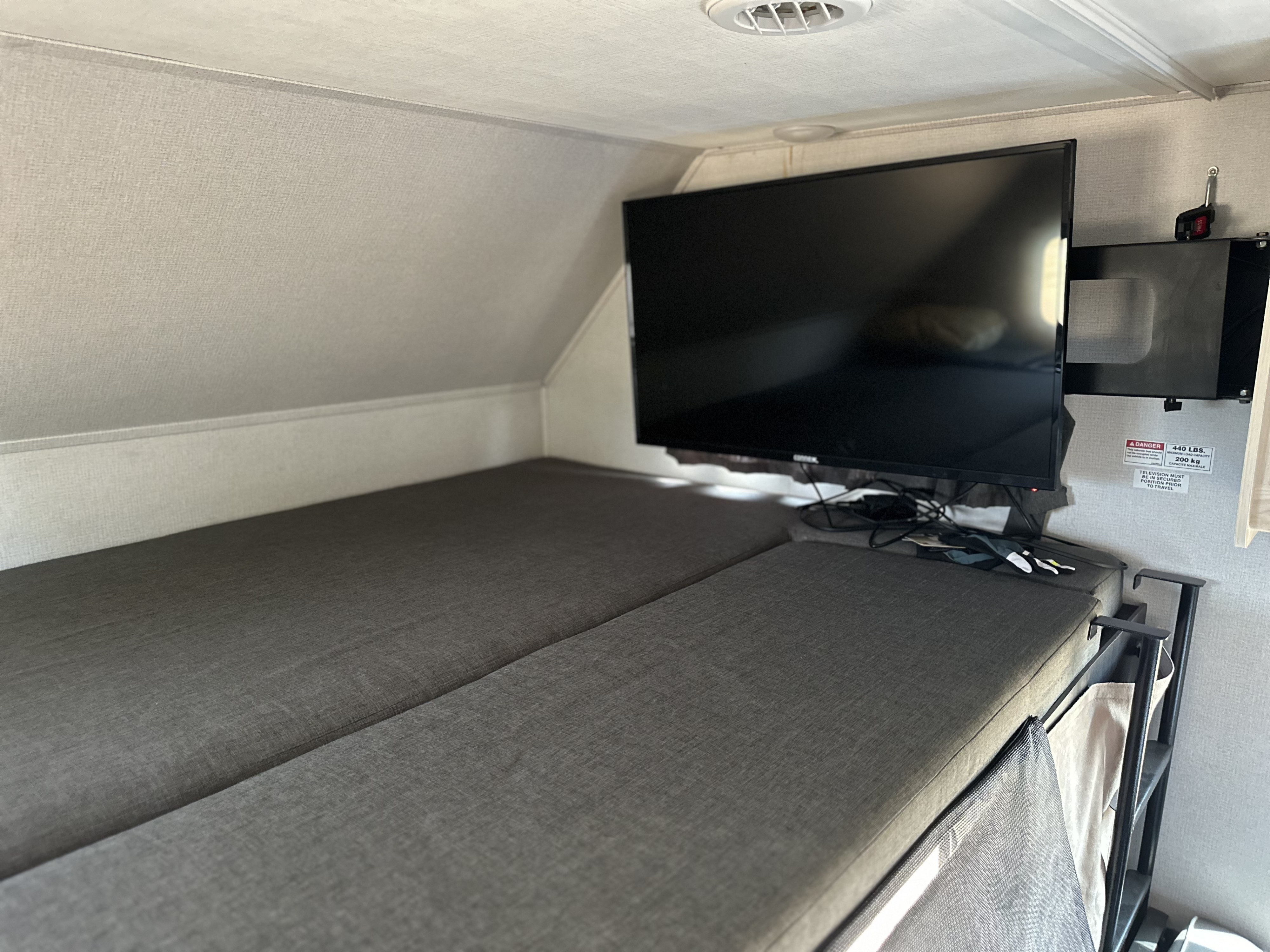 Inside an RV rental: two gray bunk beds with a wall-mounted TV overhead. A 440lb capacity label is visible.. Forest River Sunseeker LE 2023