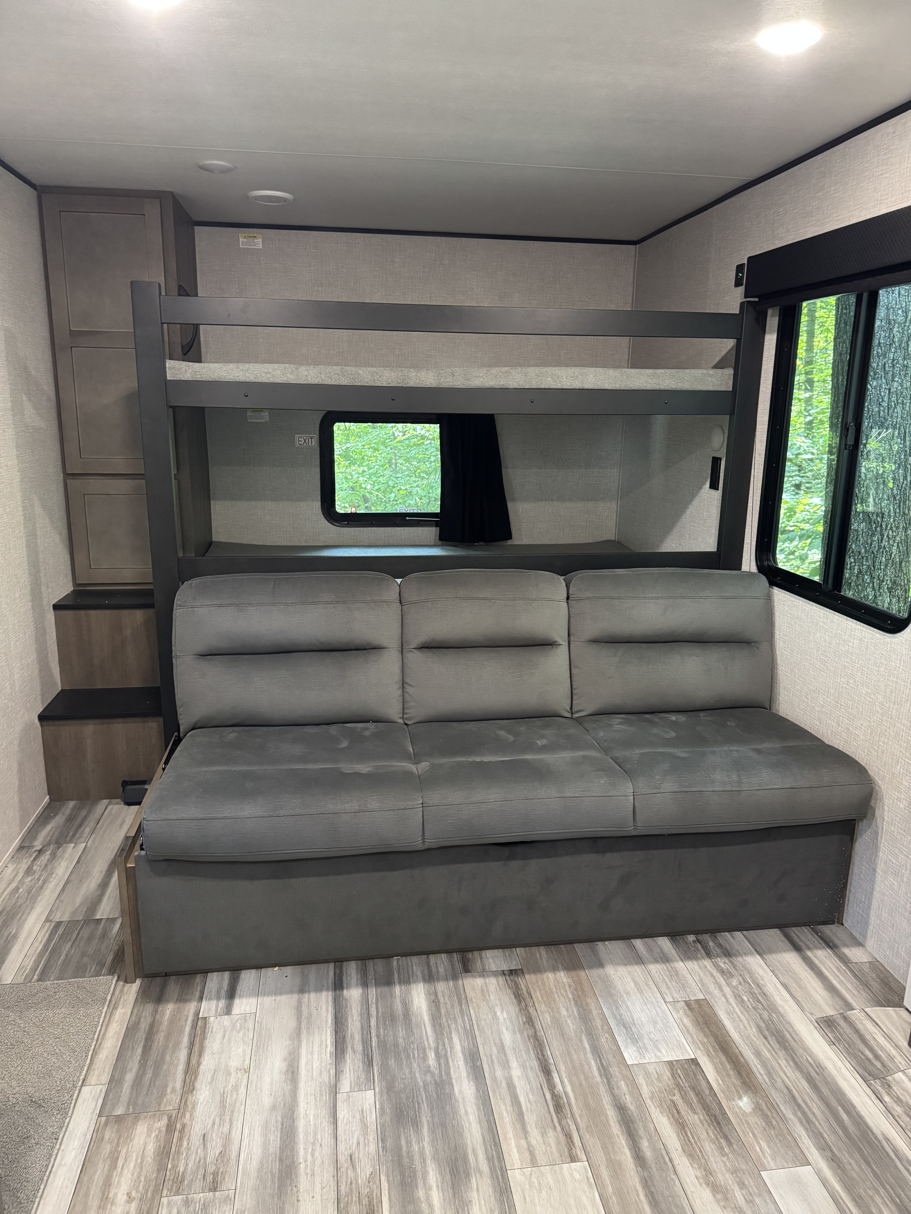 Spacious RV rental interior with comfortable bunk beds, a pull-out sofa, and a window offering a lush green view.. Jayco Jay Flight SLX 2025