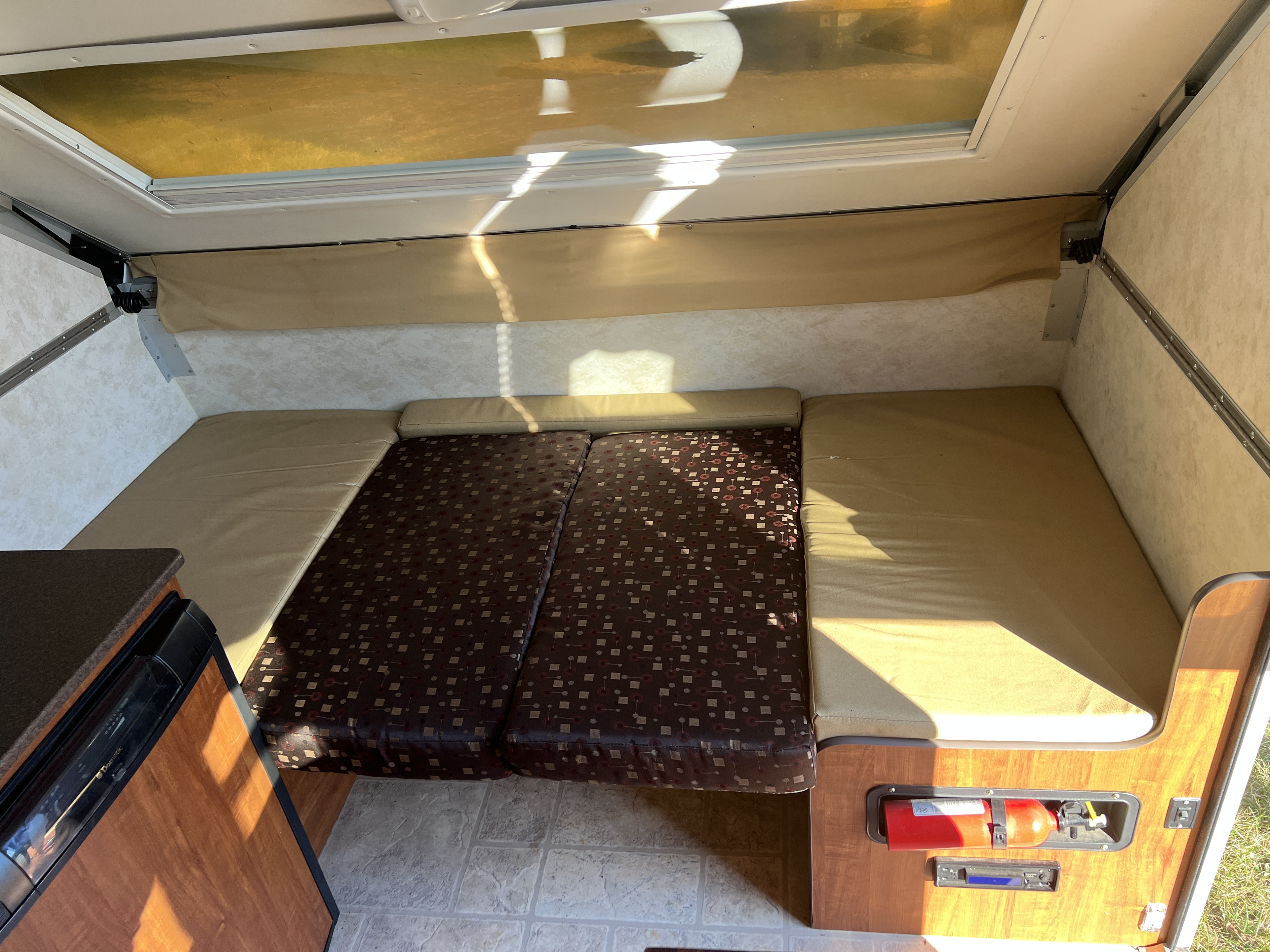 RV rental interior: light-filled space with cushioned seating, a small kitchen, and safety features like a fire extinguisher.. A Liner A Liner Popup Trailer 2013