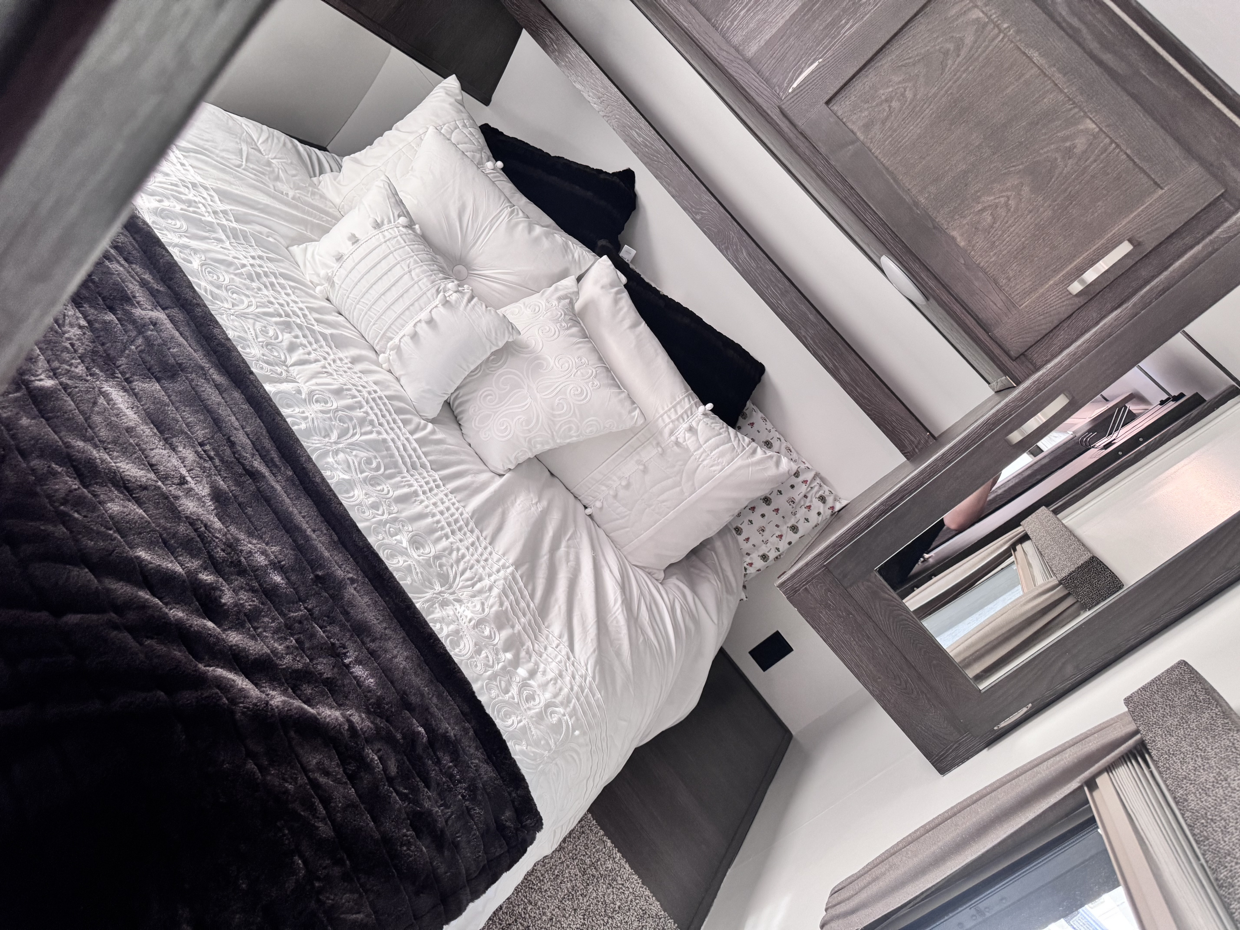 Bright RV rental bedroom with white quilted bedding, varied decorative pillows, dark throw blanket, and modern wood cabinets/mirror.. Keystone RV Outback Ultra-Lite 2018