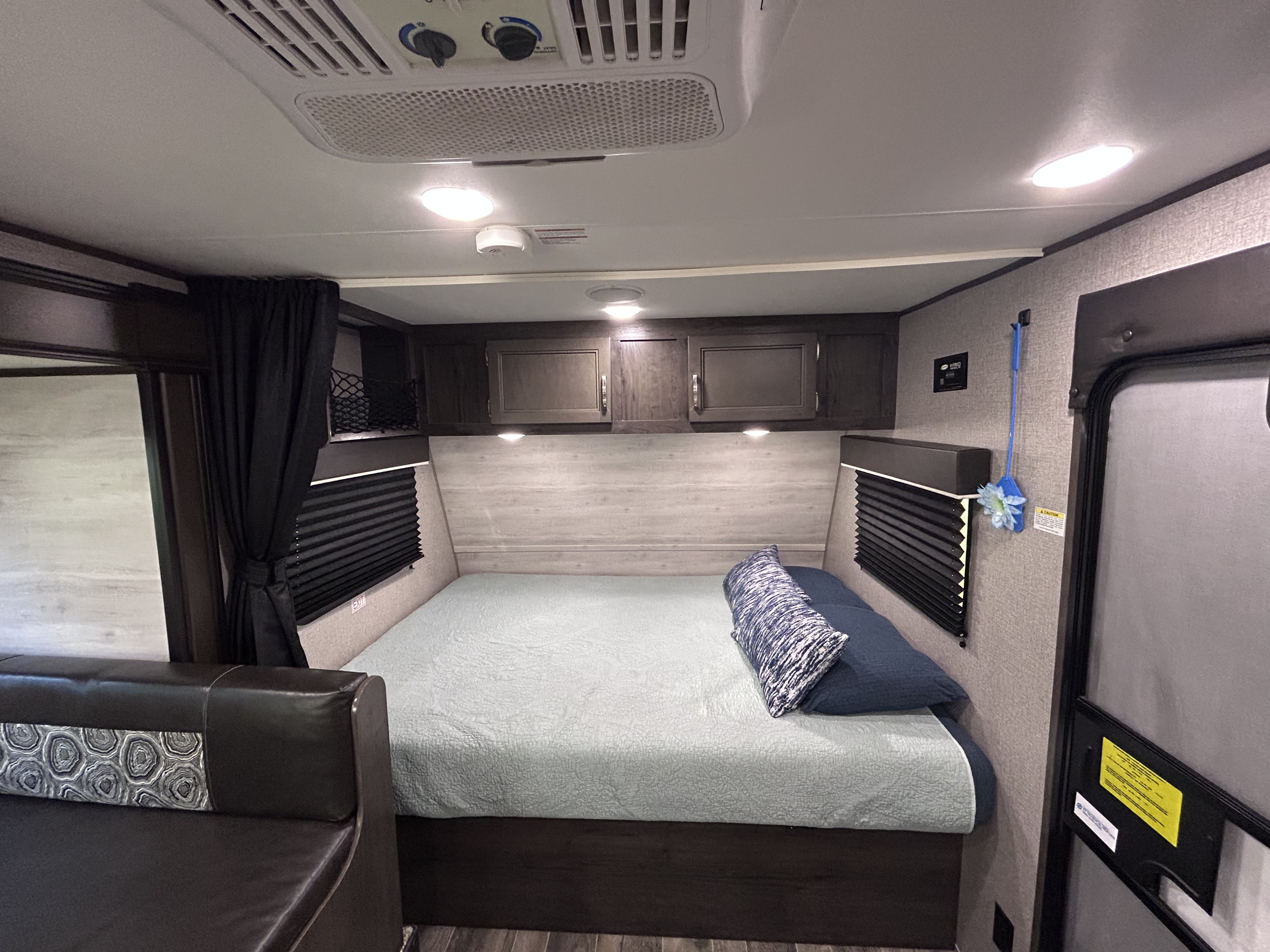 Cozy RV rental bedroom featuring a comfortable bed, overhead storage, AC unit, and seating for comfortable travel adventures.. Jayco Jay Flight SLX 2021