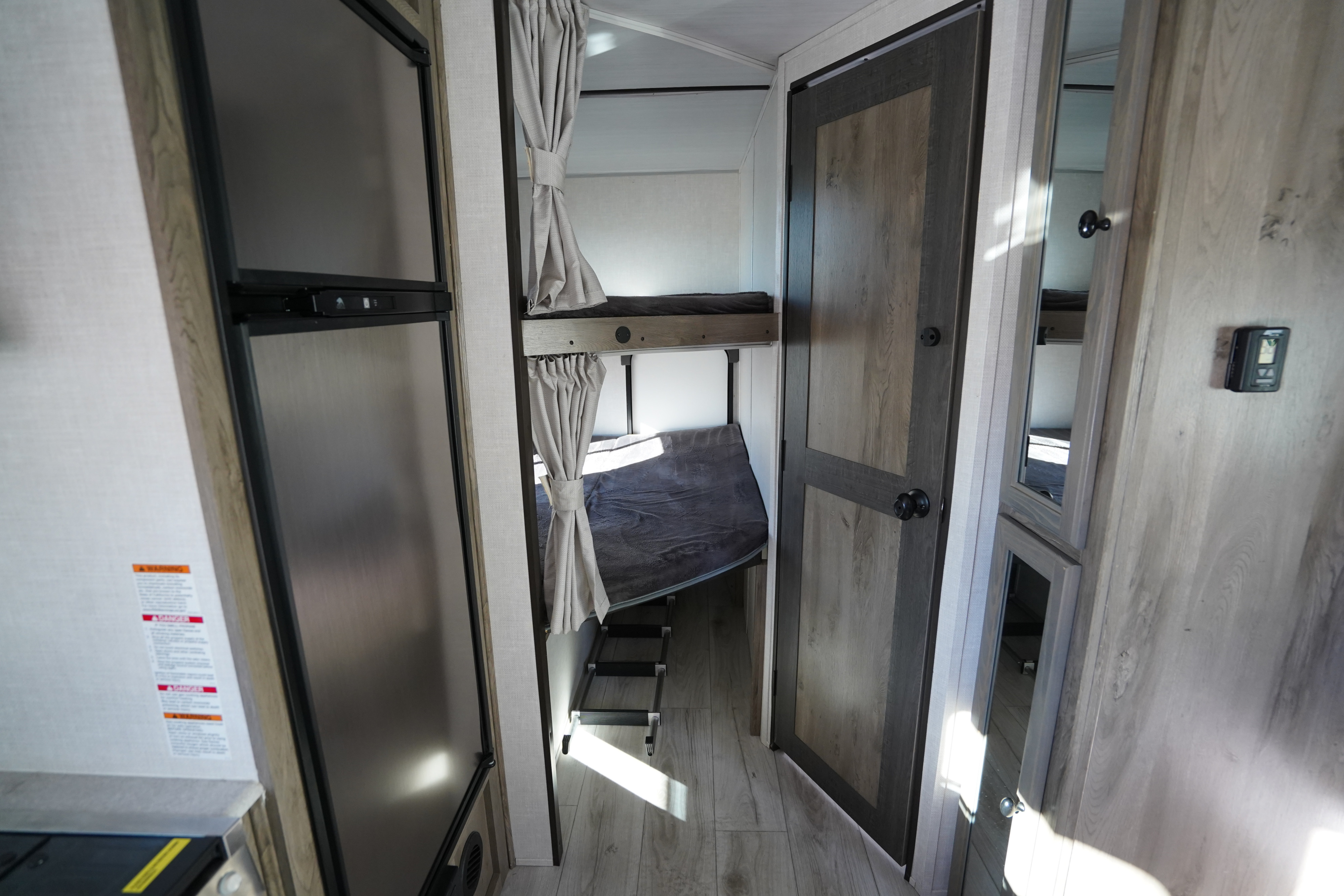 This RV rental interior features comfortable bunk beds with privacy curtains, a refrigerator, and a wooden door.. Forest River Surveyor Legend 2022