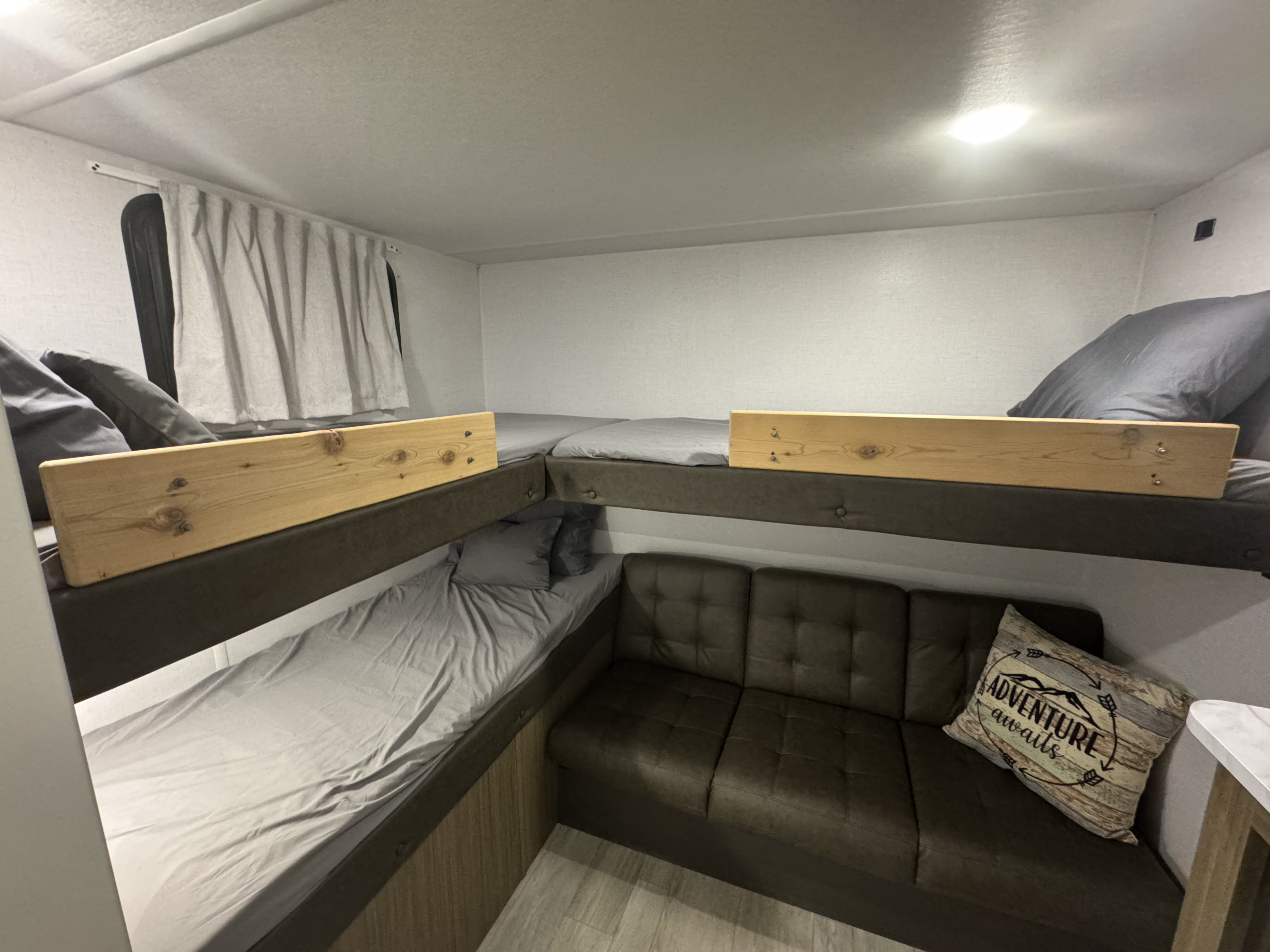 RV rental interior featuring bunk beds with wooden safety rails and a cozy L-shaped sofa, ideal for family adventures.. Forest River X-Lite 2026