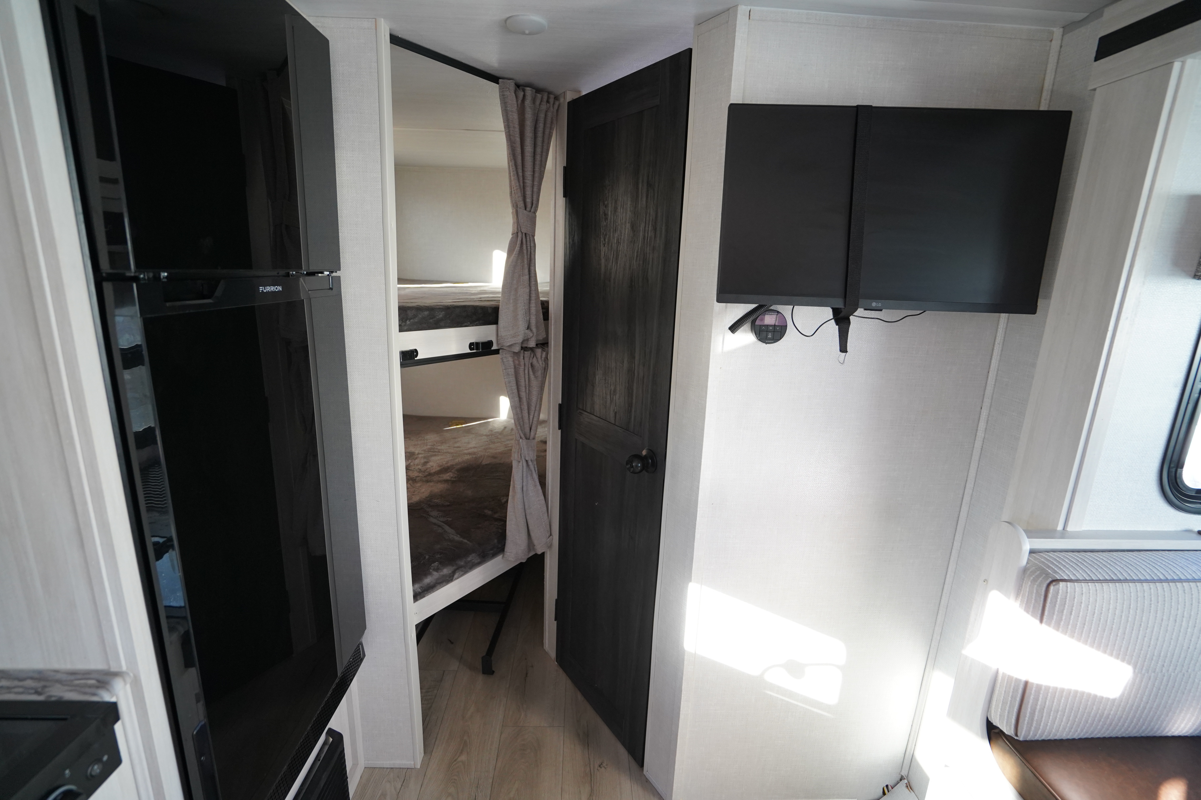 Interior of an RV rental: Furrion fridge, bunk beds with curtain, dark door, and mounted TVs.. Forest River Surveyor Legend 2024