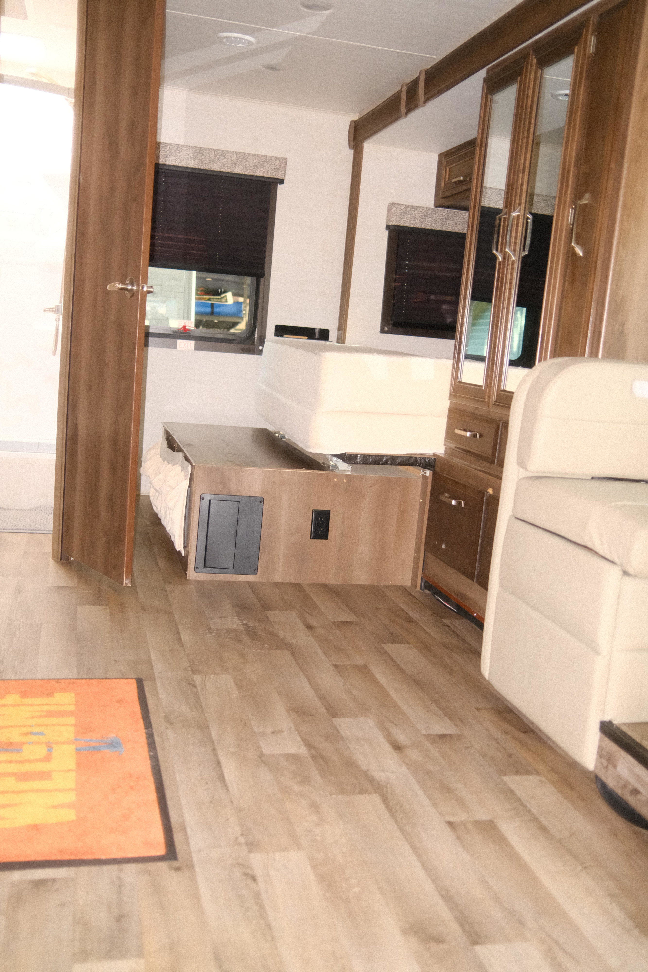 RV rental interior: compact living space with light wood floor, transforming bed/sofa, windows, and cabinetry.. Jayco Melbourne Prestige 2021
