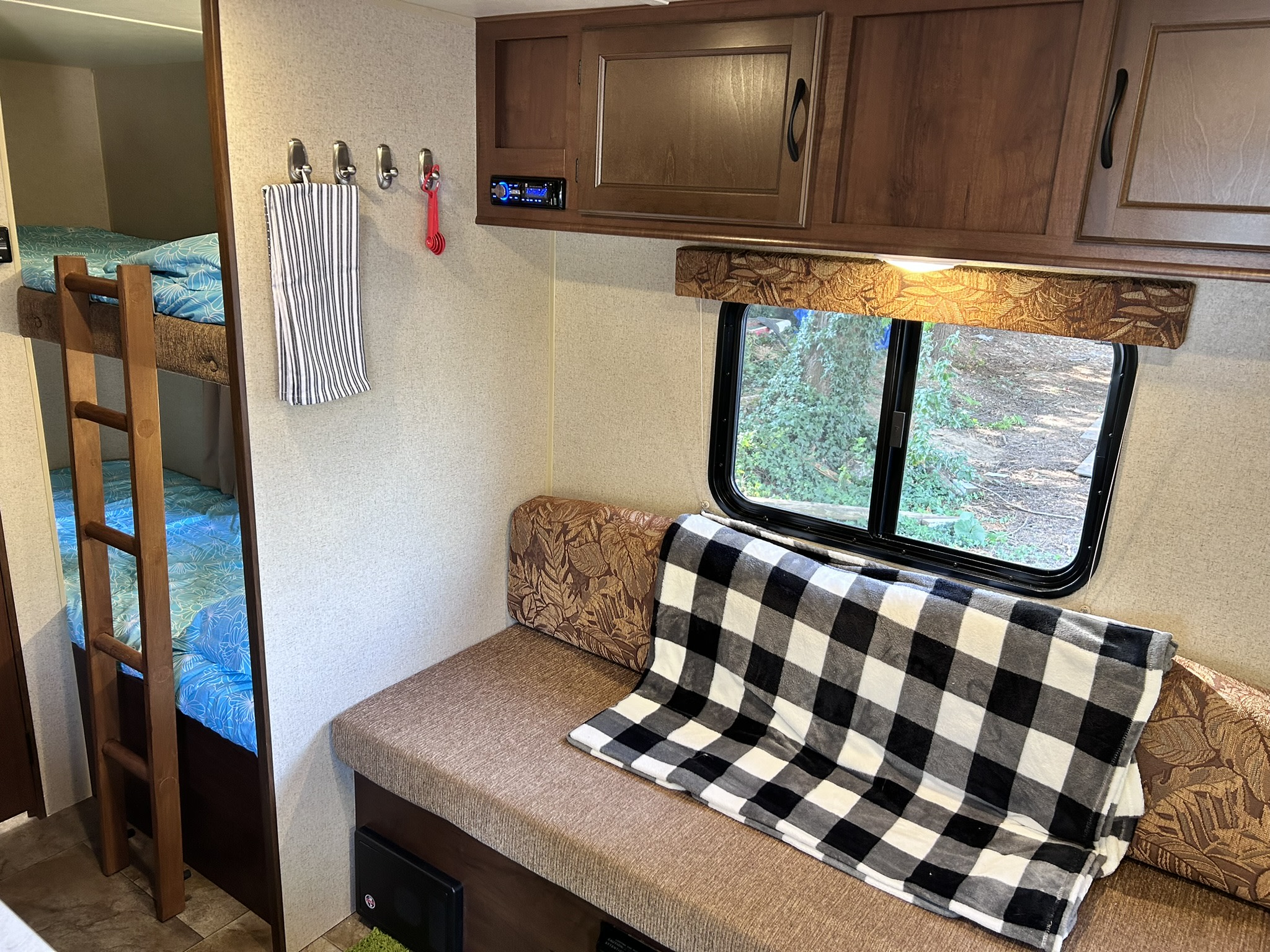 Cozy RV rental interior showcasing bunk beds, a dinette with a plaid blanket, overhead cabinets, and window.. Jayco Jay Flight SLX 2015