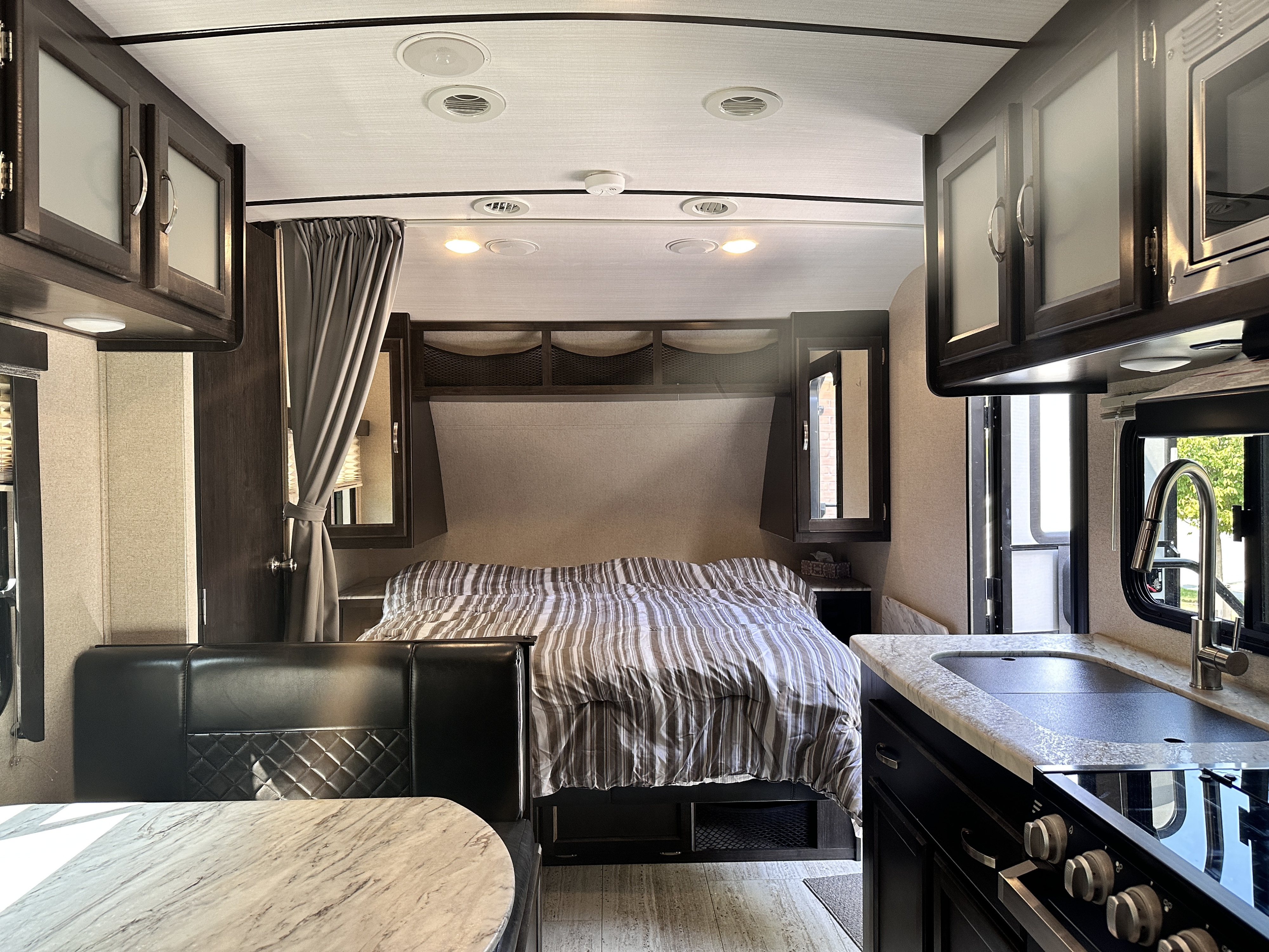 Inside a modern rv rental showing a bedroom with striped bedding, kitchen with sink & stove, and dining bench. Functional and cozy.. Forest River Coachmen Spirit Ultra Lite 2019
