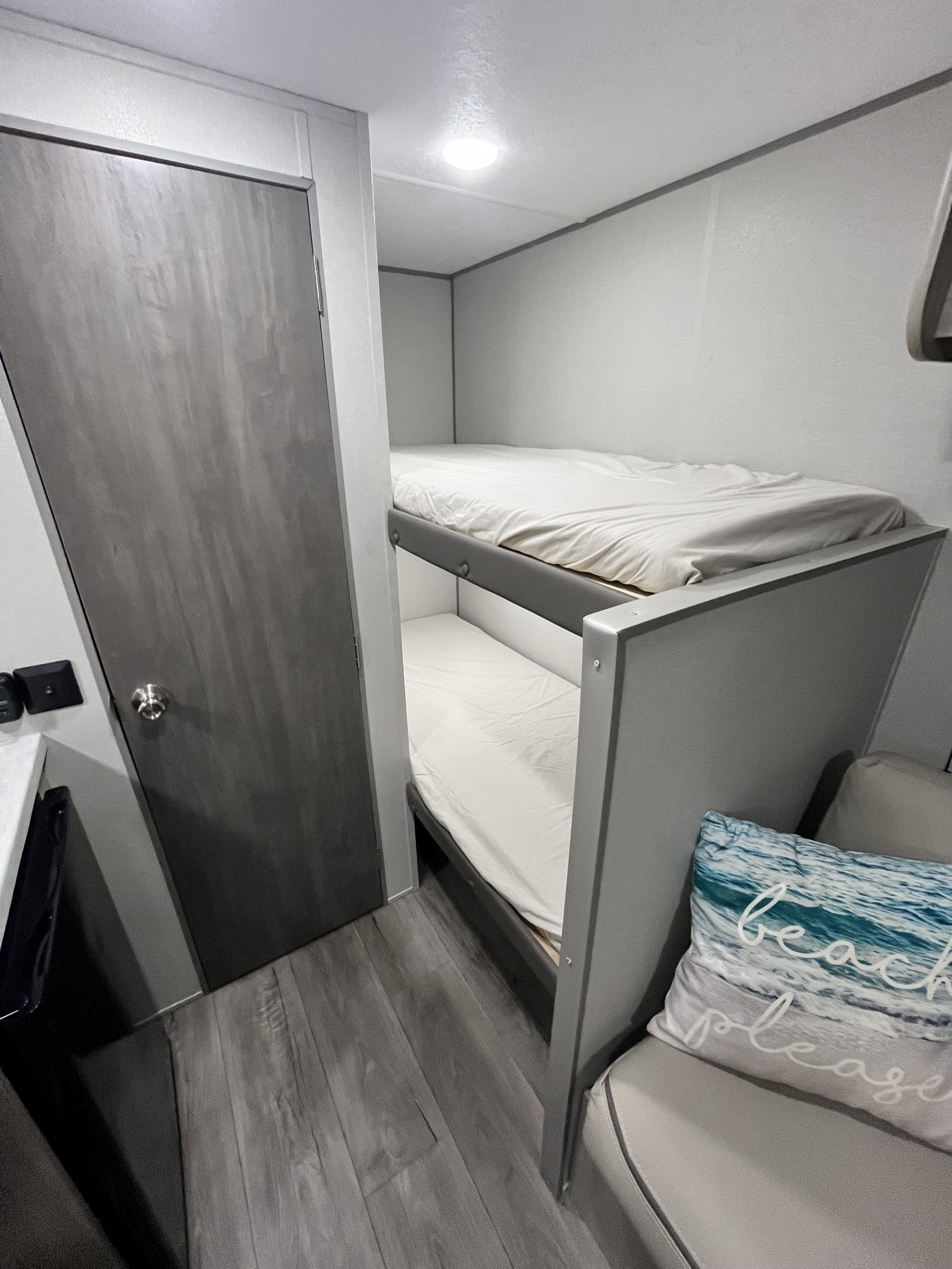 Compact RV rental interior: modern gray bunk beds, a light wood-look floor, and a closed door in a cozy space.. Coachmen Catalina Summit 164BHX 2024